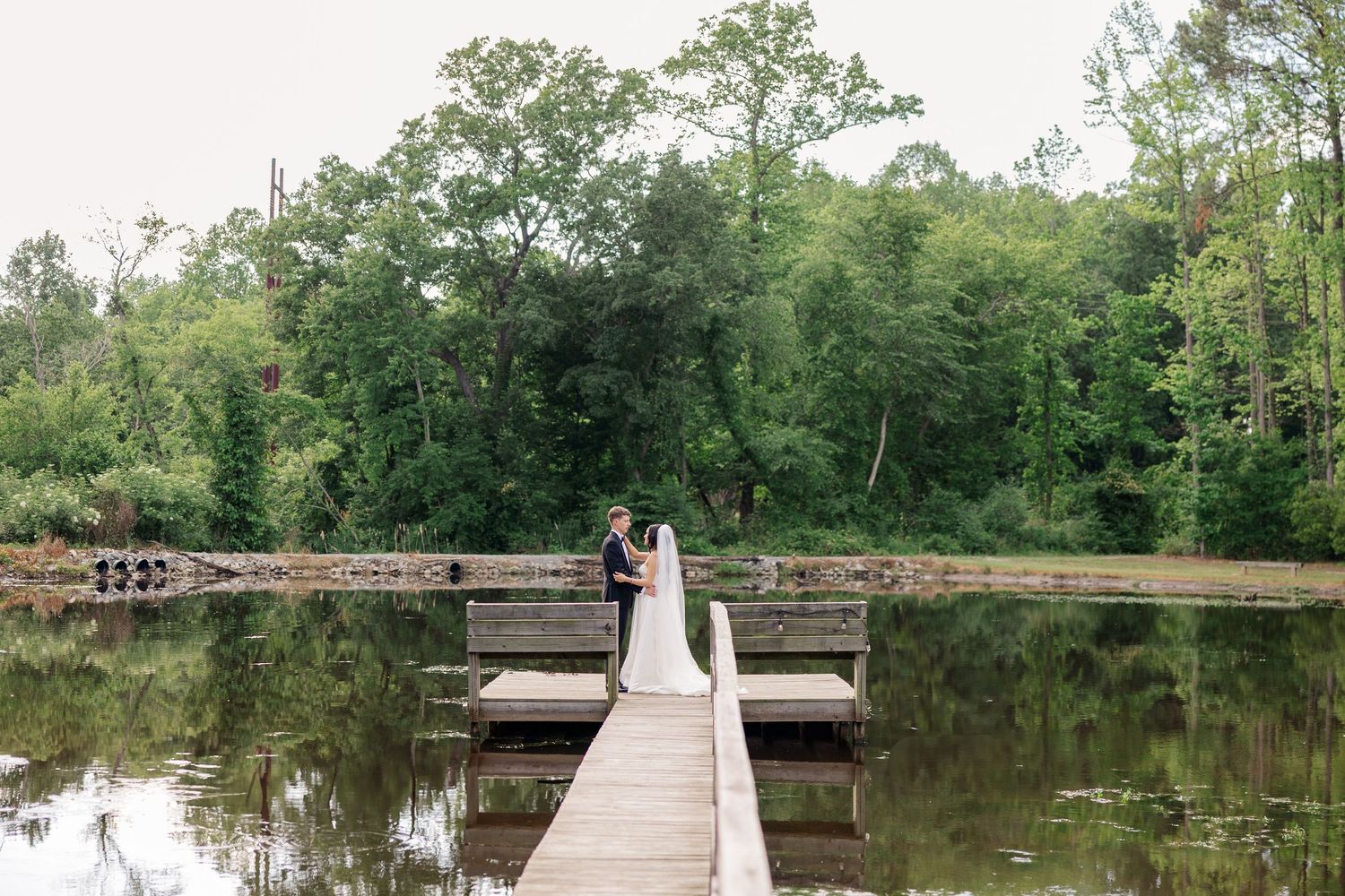 Long wooden dock extending over a serene lake surrounded by green trees.