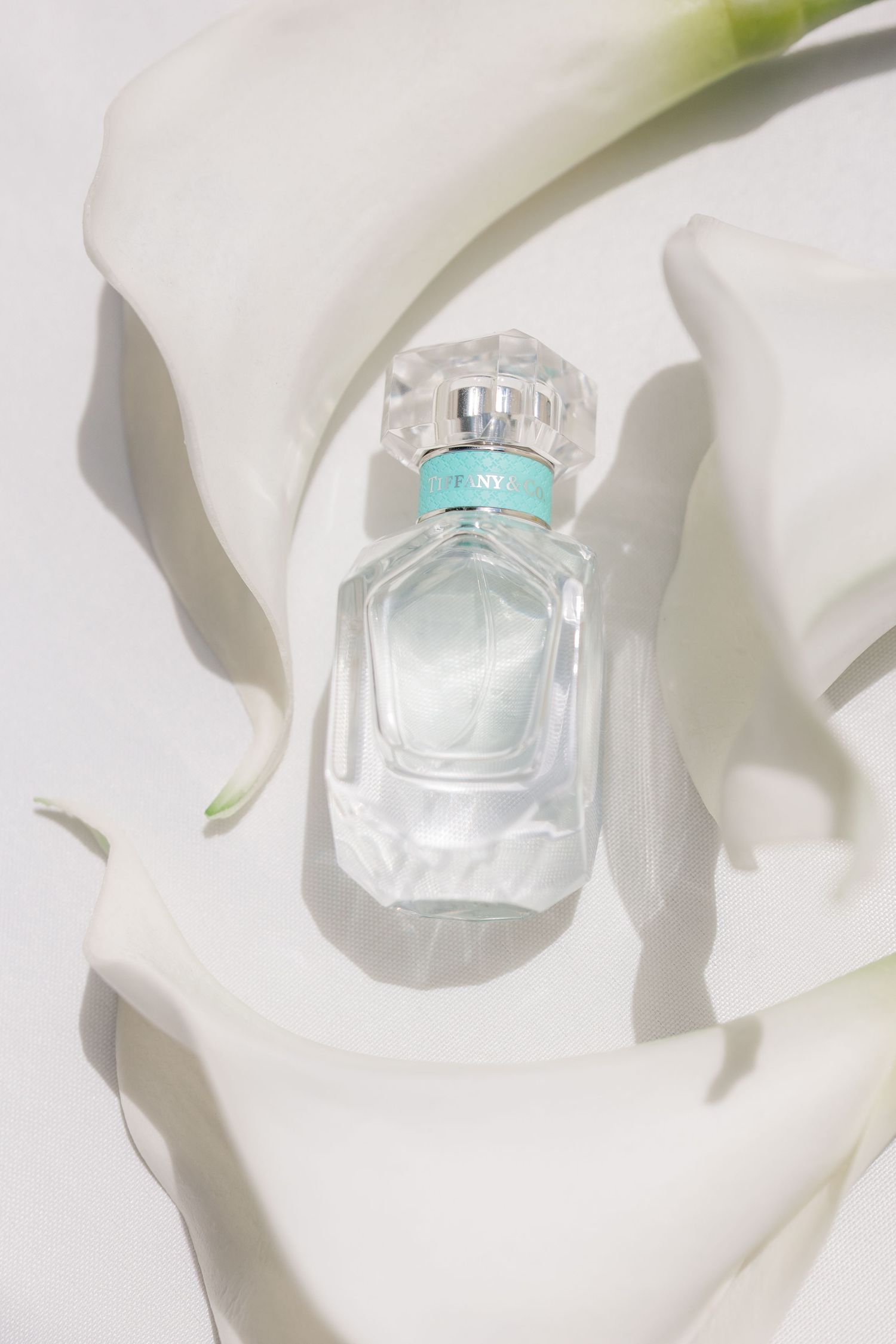 Elegant perfume bottles with iridescent design displayed on white fabric with soft shadows.