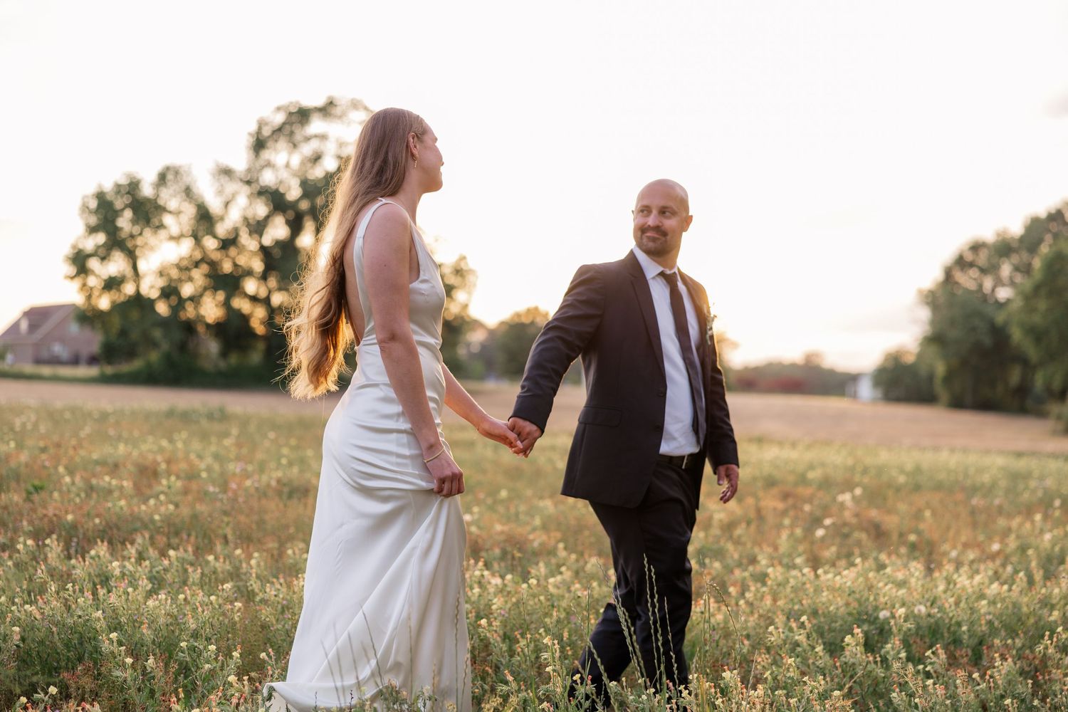 Wedding couple shares playful moments in a sunlit field during golden hour.
