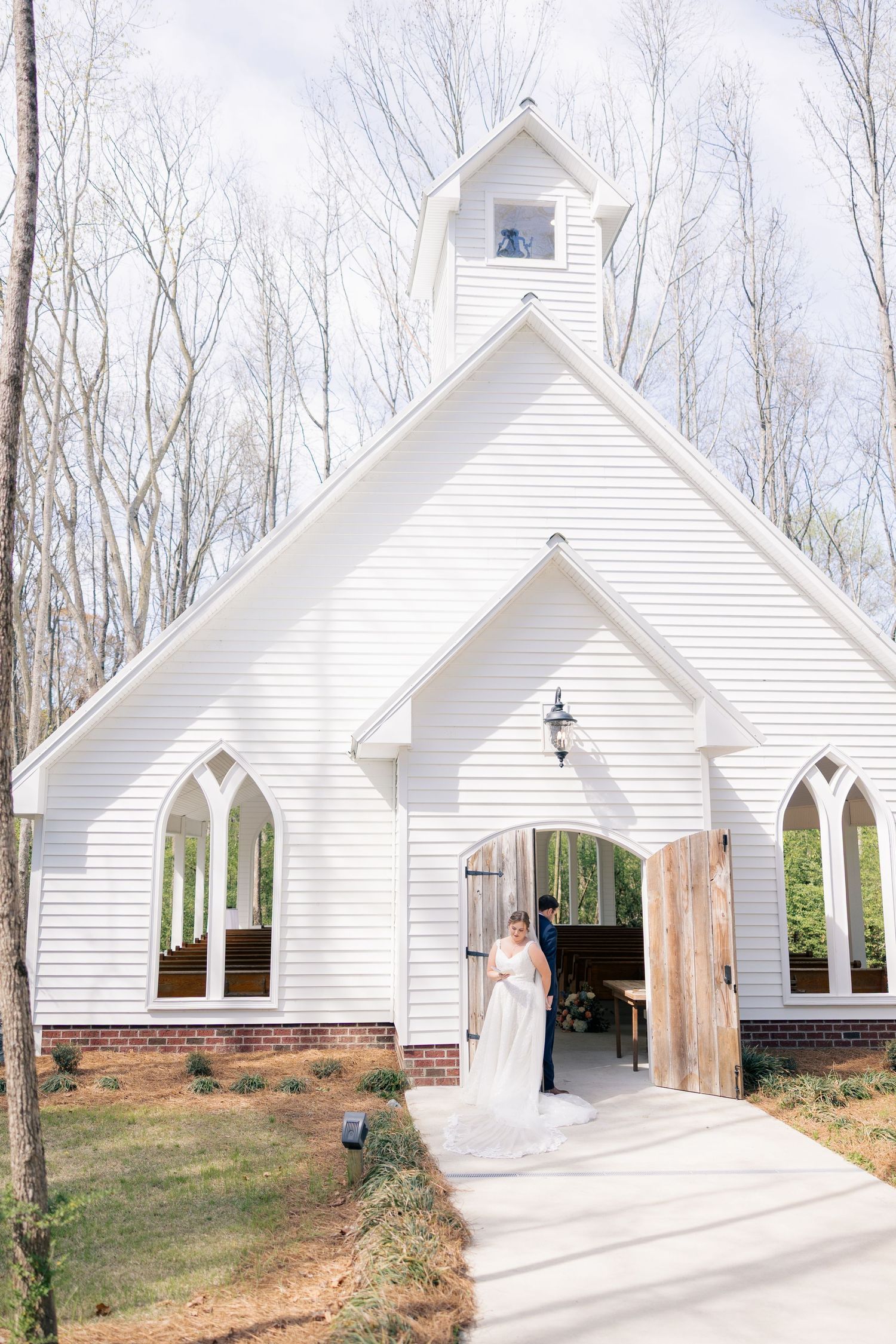 White wedding chapel exterior with gothic arched windows nestled among trees at a woodland venue.