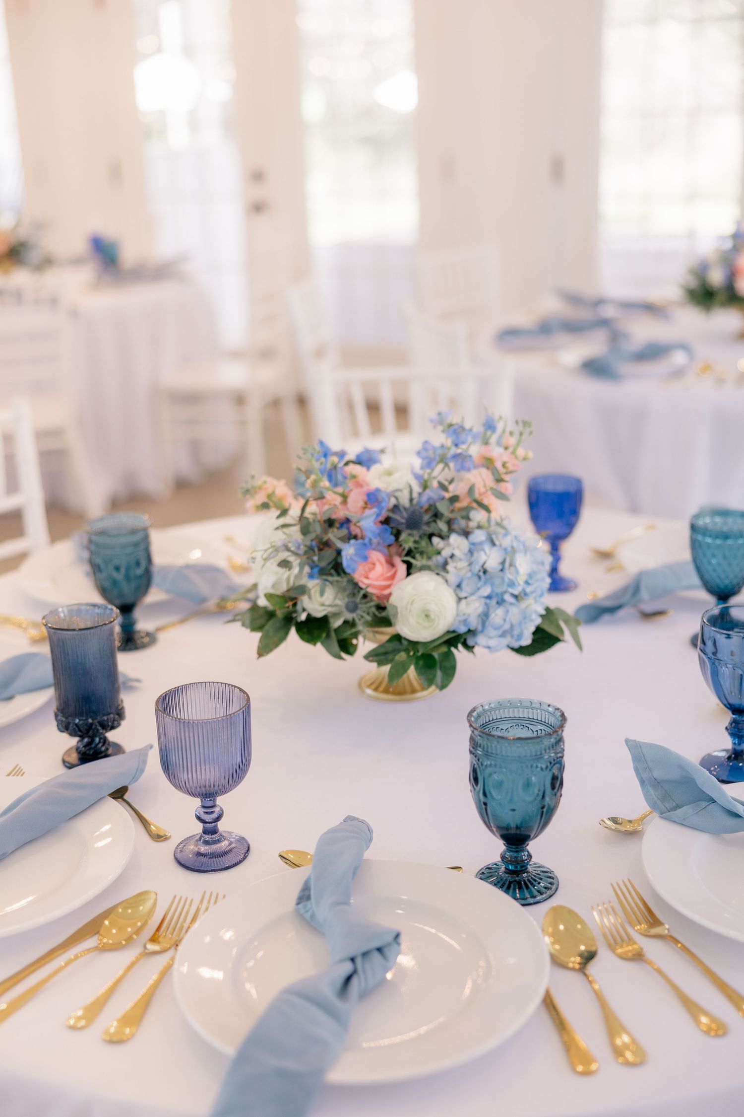 Elegant table settings featuring blue glassware, gold cutlery, and delicate floral centerpieces at a wedding reception.