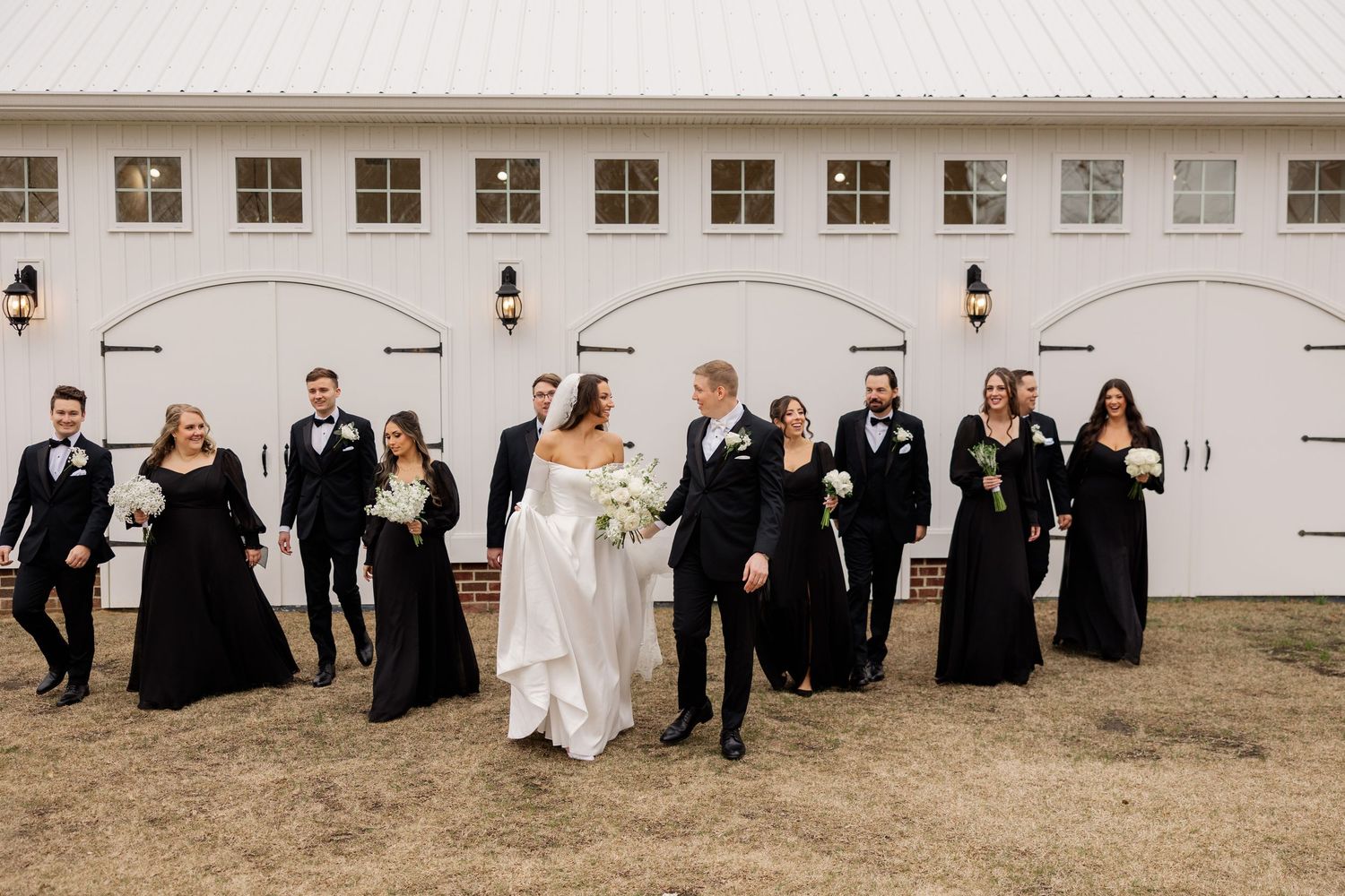Wedding party in formal black and white attire poses together outside venue.
