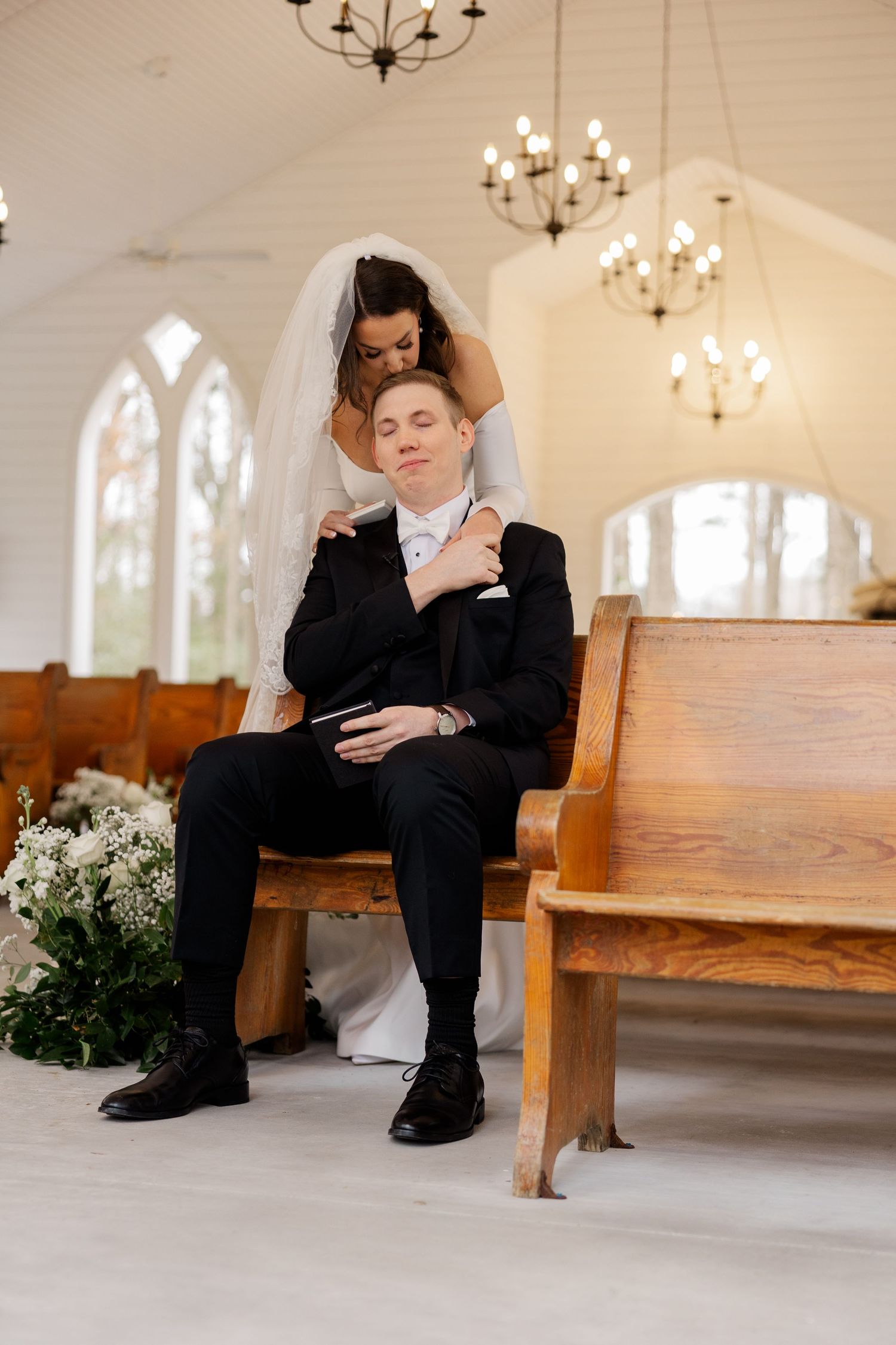 White wooden chapel interior with chandelier and wooden pews decorated for a wedding ceremony.