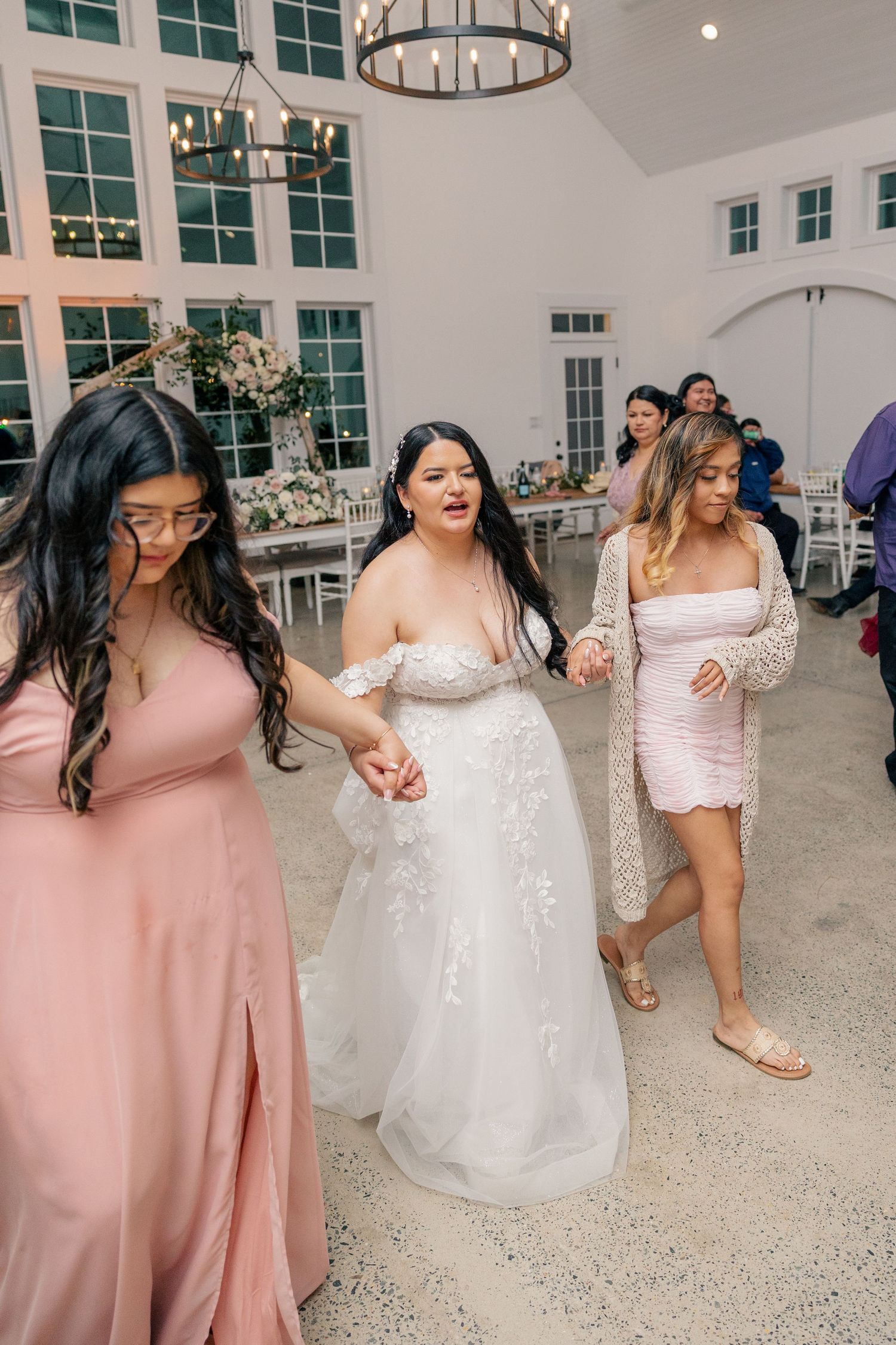 Wedding party in pink bridesmaid dresses and white bridal gown dancing at reception.