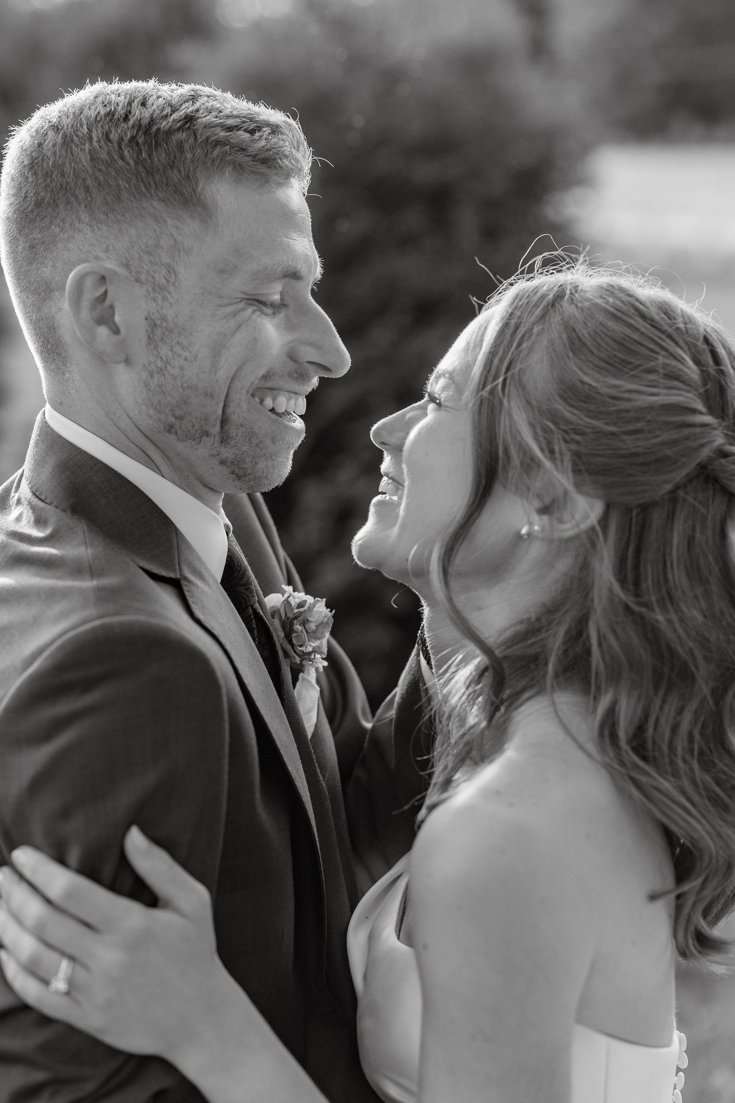 Black and white photo of smiling bride and groom embracing outdoors on their wedding day.