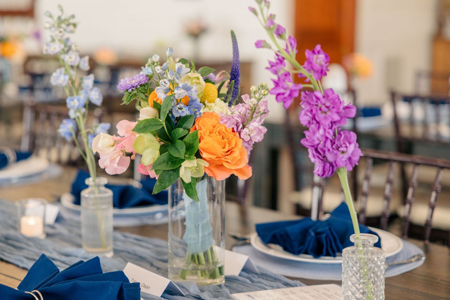 Elegant wedding reception table with colorful floral centerpieces and navy blue napkins.