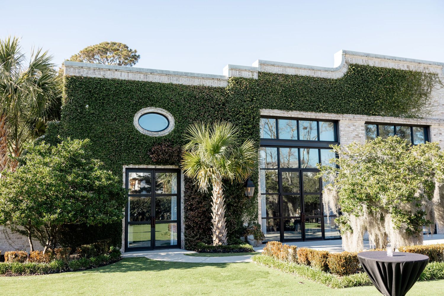 Modern commercial building exterior with green living wall facade, large windows and palm trees in landscaping.