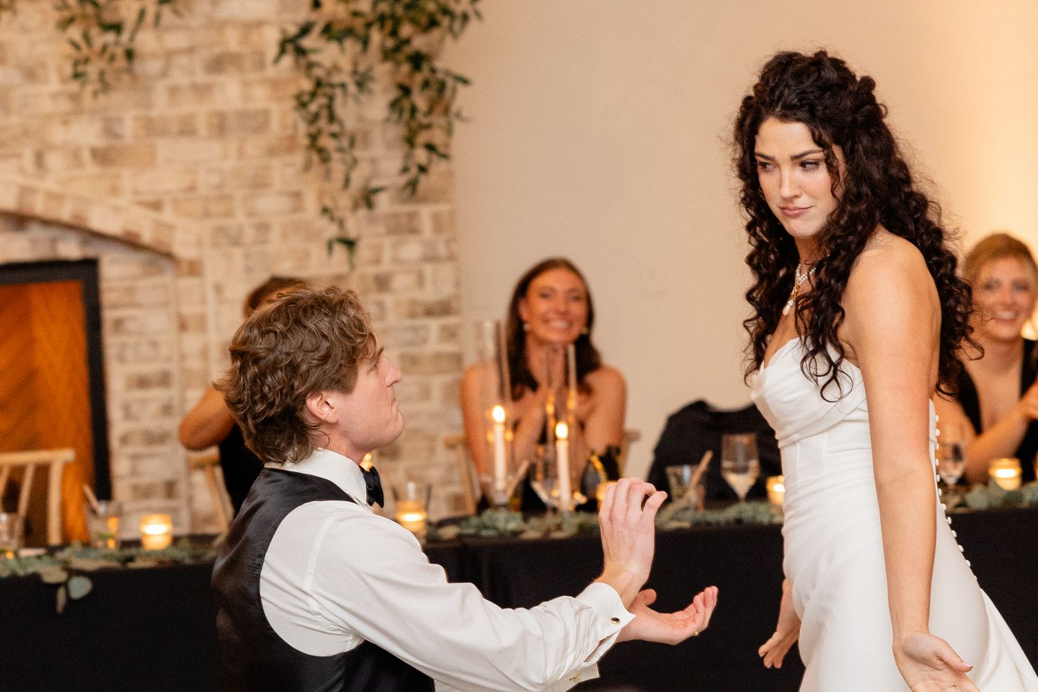 A couple sharing a playful moment during their wedding reception by a brick wall.