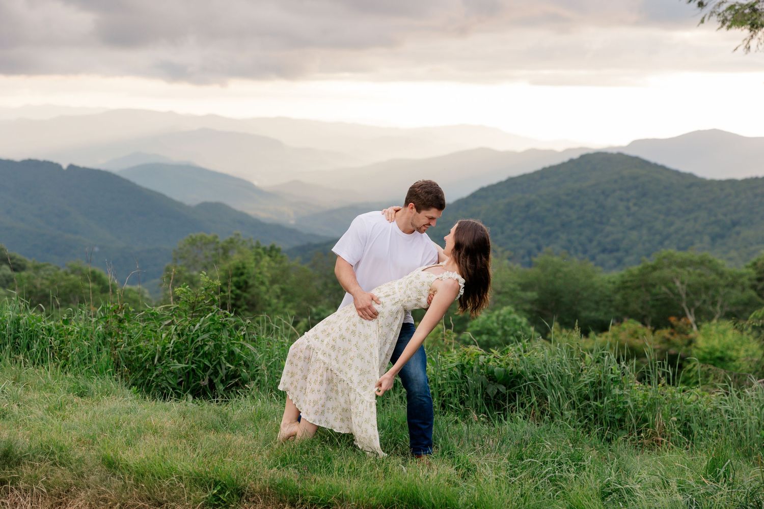 Blue Ridge Parkway wedding photographer. A romantic couple embraces against a backdrop of misty mountain peaks and green fields.