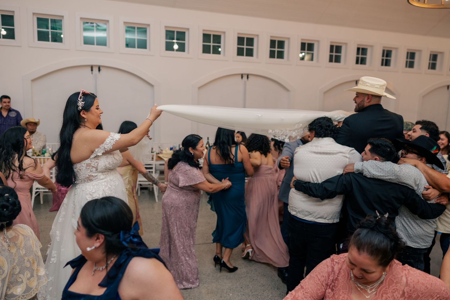 Wedding guests dance and celebrate together on a packed dance floor at an indoor reception venue.