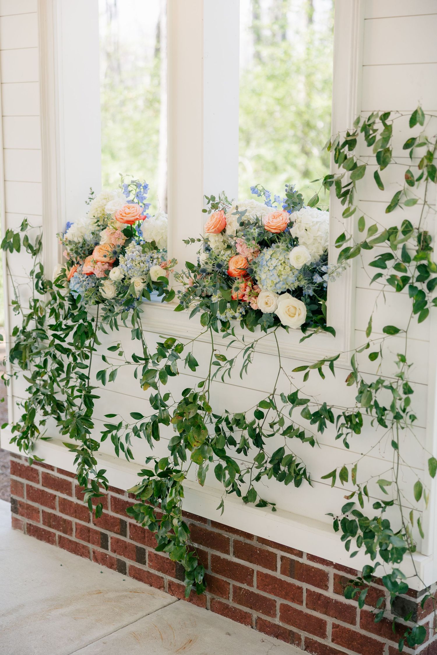 Beautiful greenery and peach rose garland adorning a brick wall in a light-filled venue.