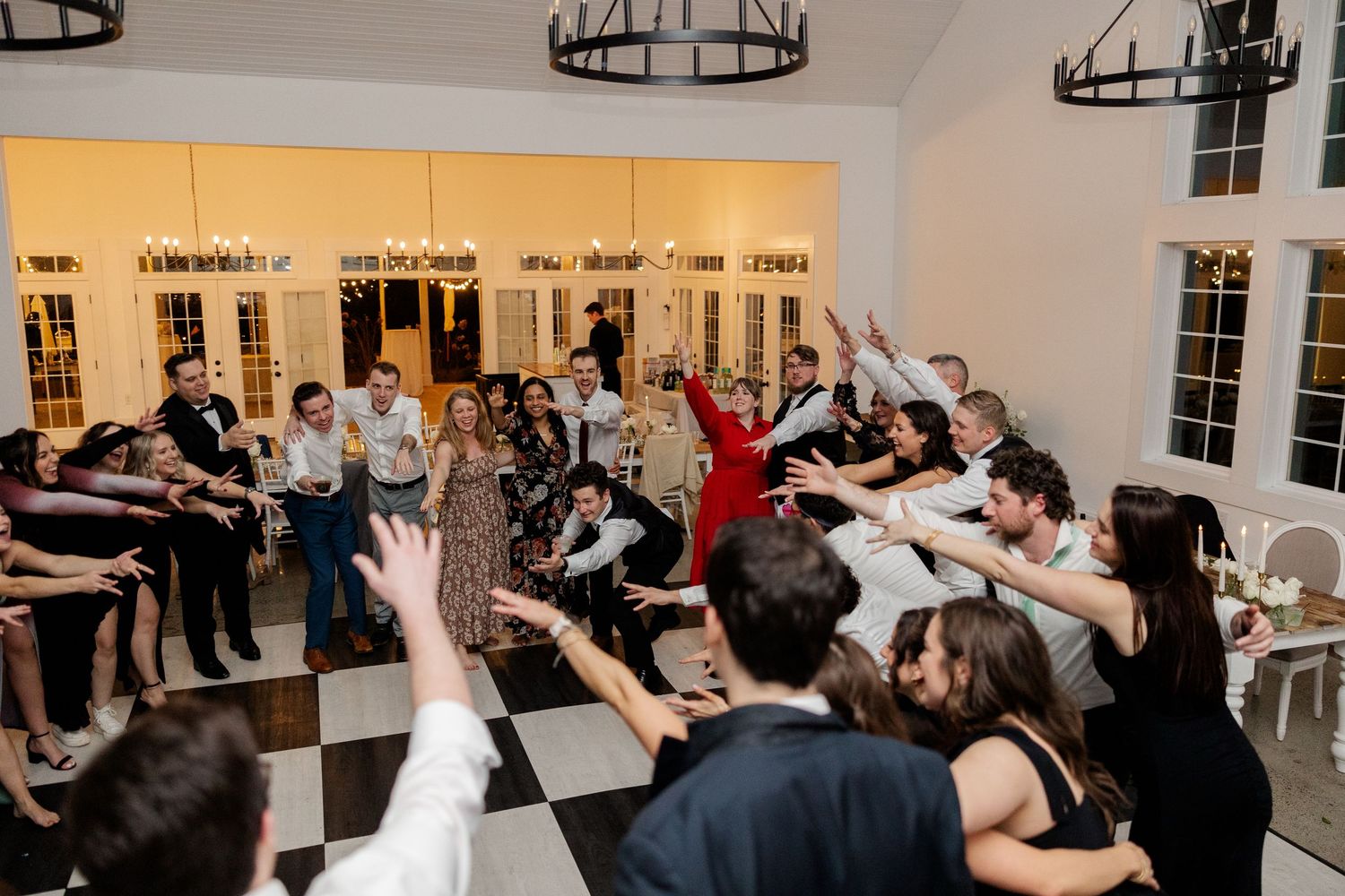 Wedding reception guests dance and celebrate with joy under modern black chandeliers.