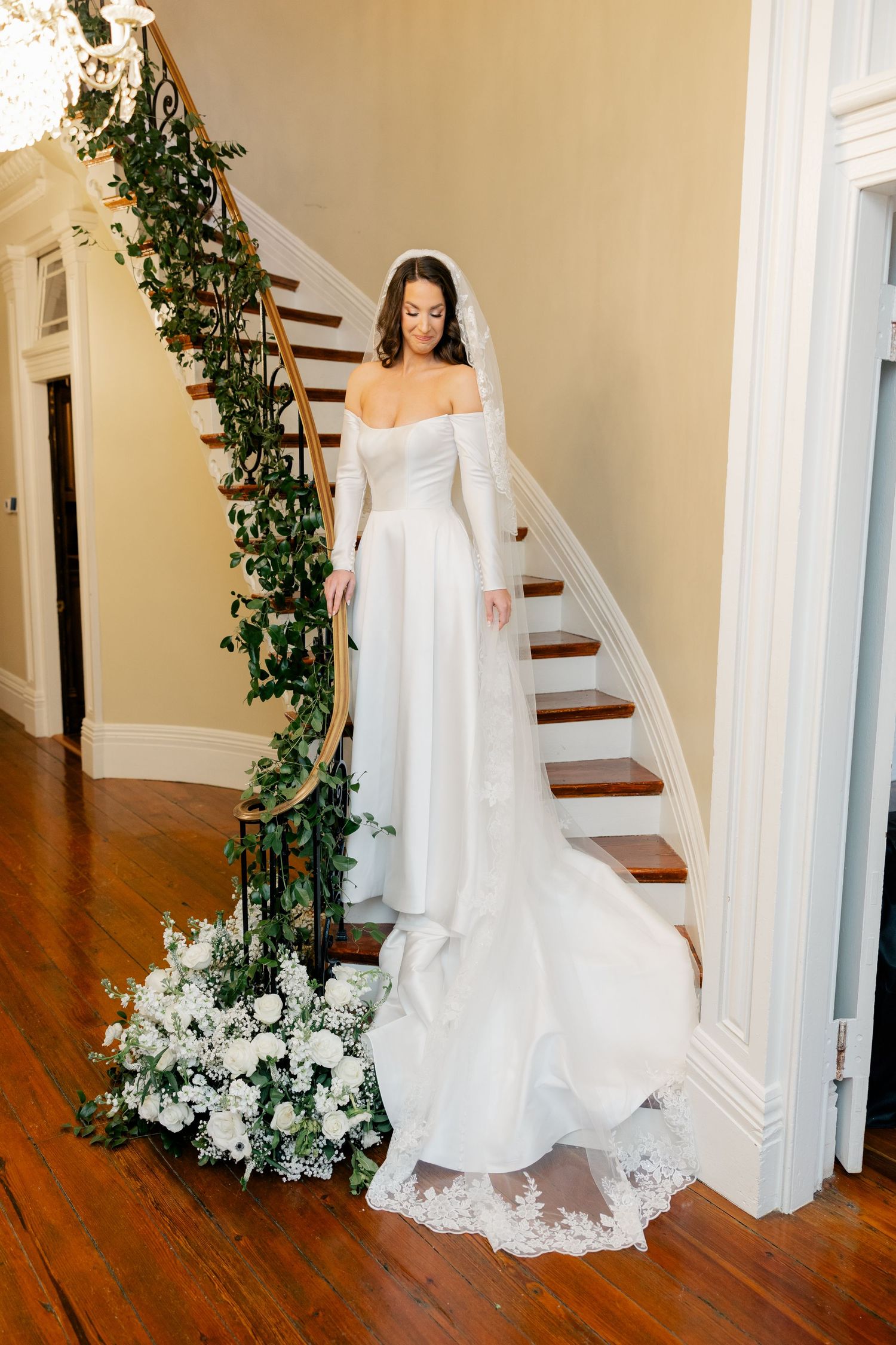 Elegant curved staircase adorned with greenery and white floral arrangements.