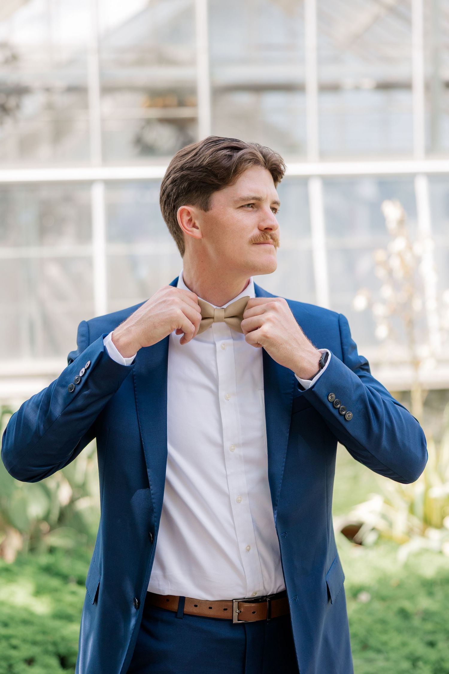 Groom adjusting tie and collar while wearing navy blue suit and white shirt.