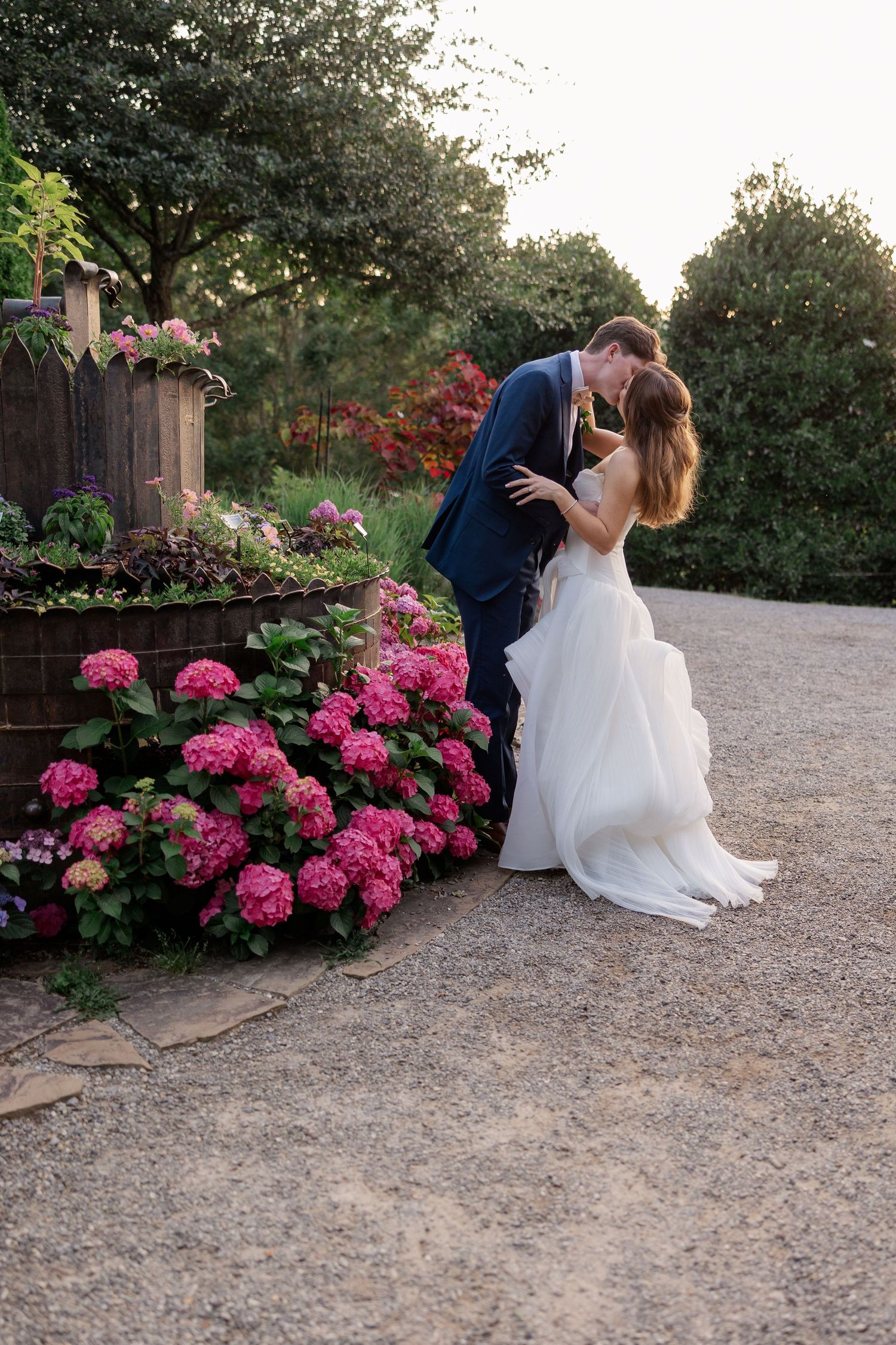 A romantic wedding moment captured among vibrant pink flowers in a garden path.