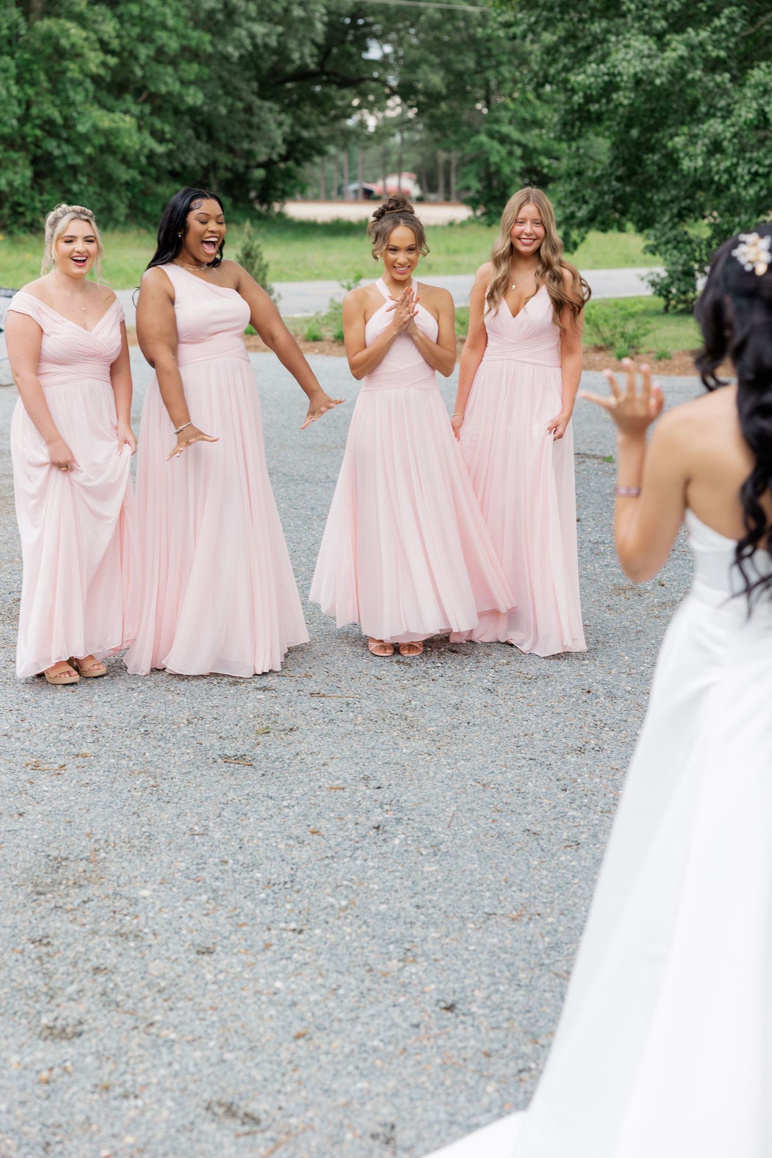 Bridesmaids in flowing pink dresses react with joy during an outdoor wedding photoshoot.