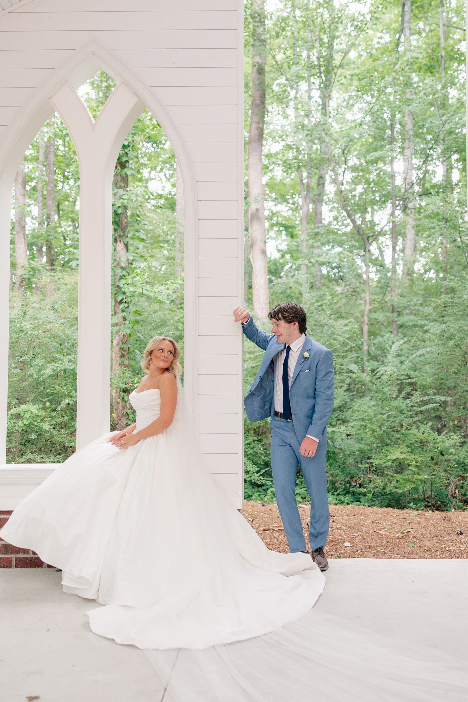 Bride and groom pose playfully by white chapel gothic arched windows.
