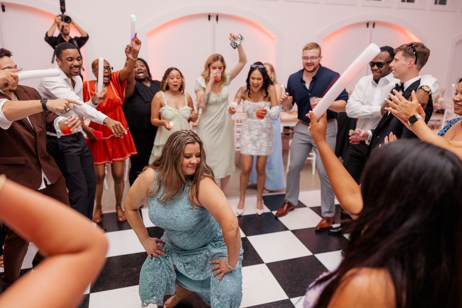 Wedding reception guests dancing and celebrating under pink neon lighting.