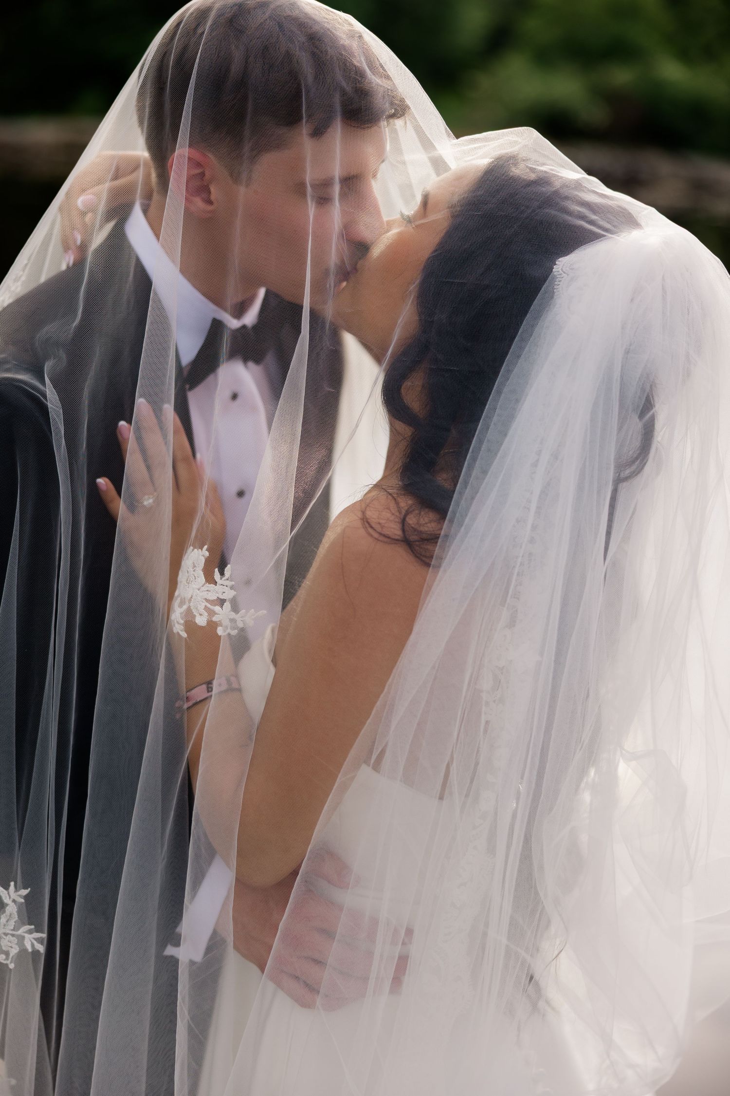 Romantic wedding kiss captured through flowing white veil against dark background.