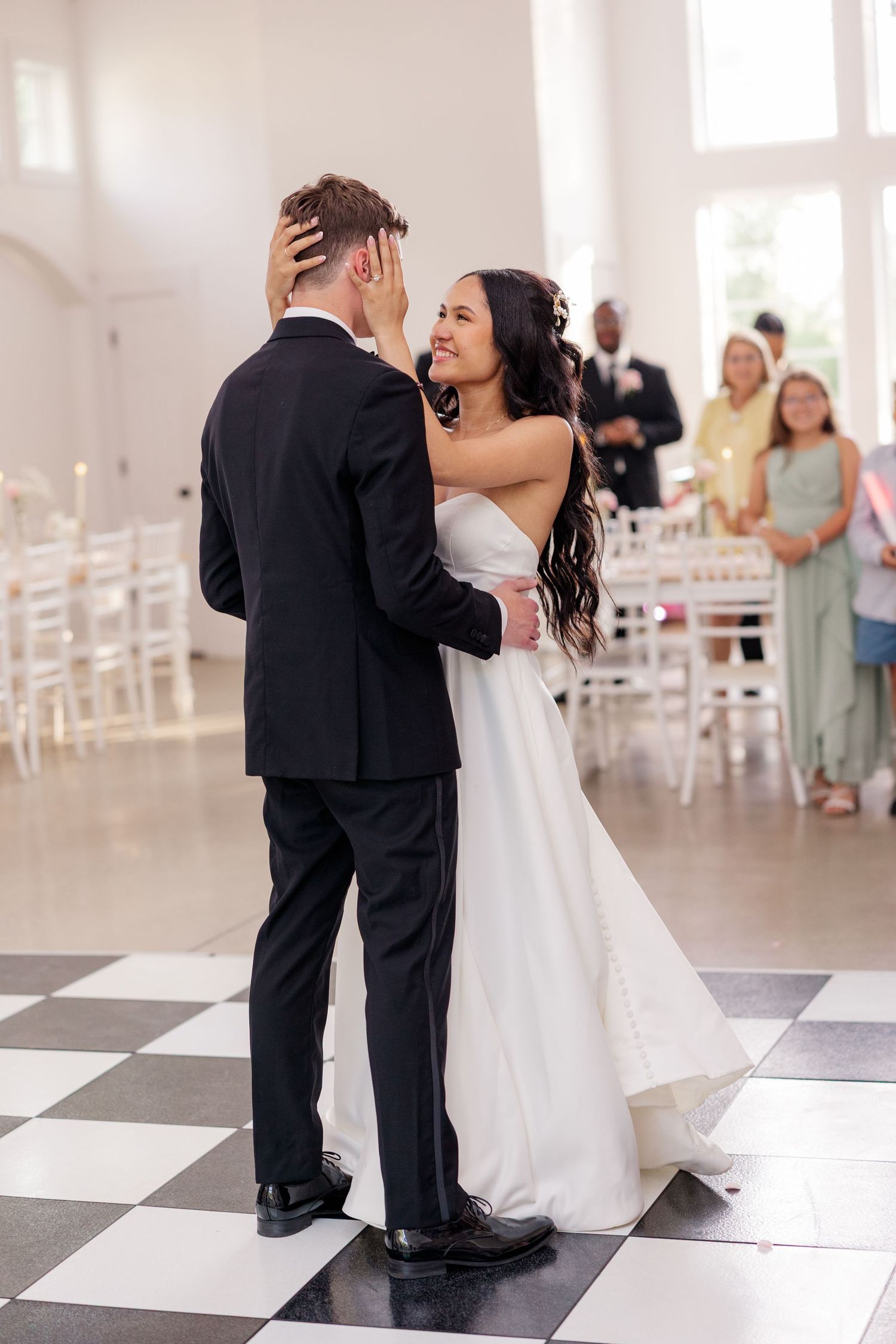 Wedding dance moment captured on a black and white checkered floor in an elegant white venue.