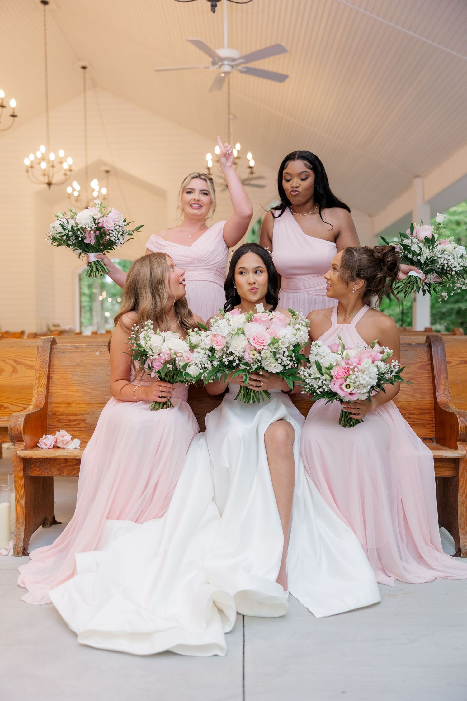 A group wearing pink and white gowns pose with floral bouquets in an elegant chapel setting.