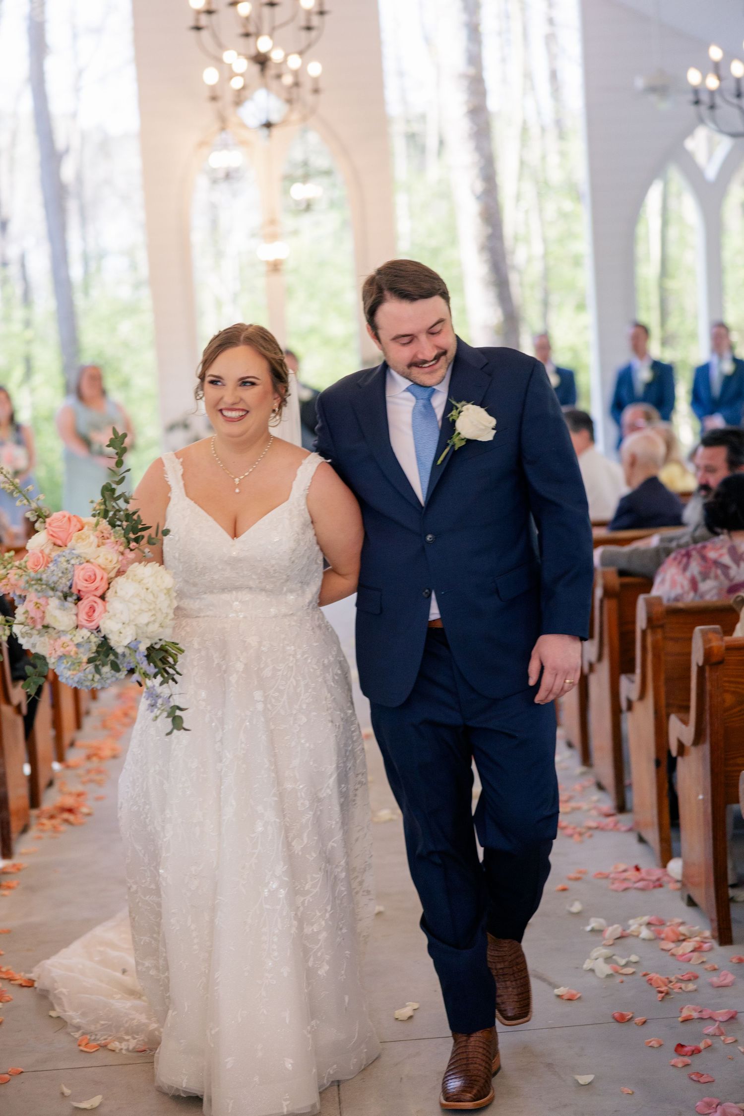 Couple proceed down chapel aisle decorated with scattered pink rose petals.