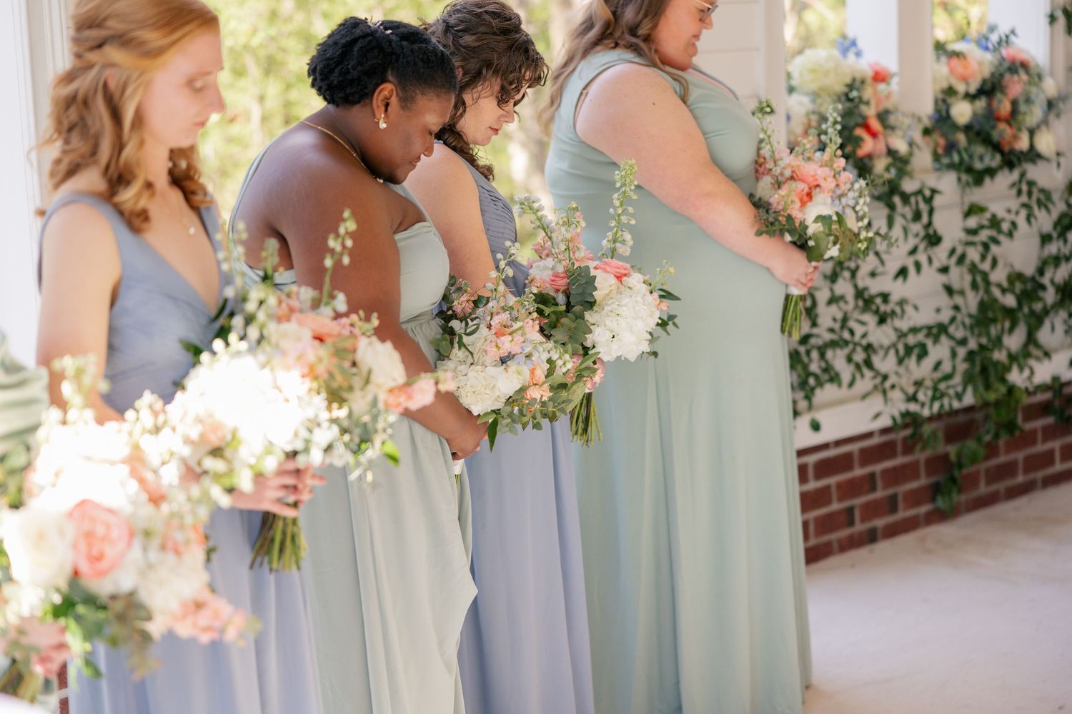 Bridesmaids in soft blue dresses hold pink and white bouquets during an outdoor ceremony.