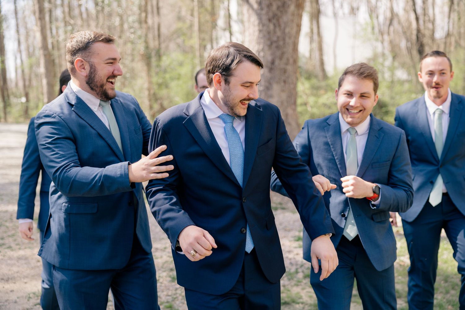 Groomsmen in matching navy suits share laughs together outdoors.