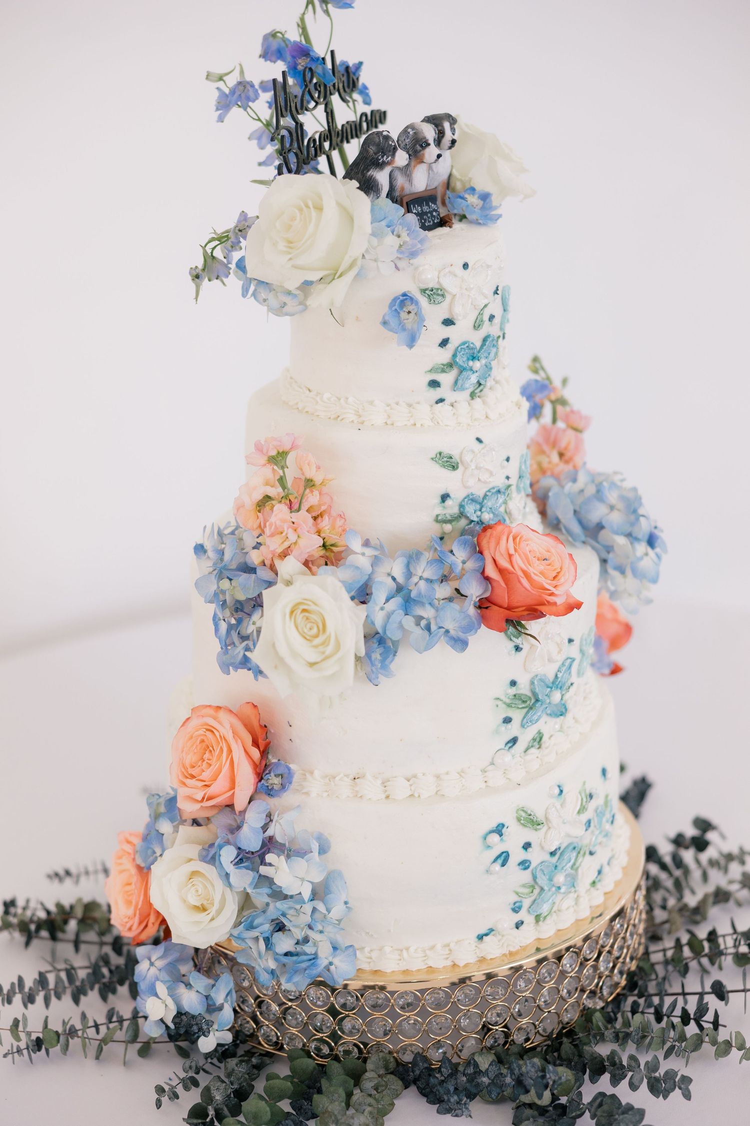 Elegant white wedding cake decorated with blue and peach flowers on display.