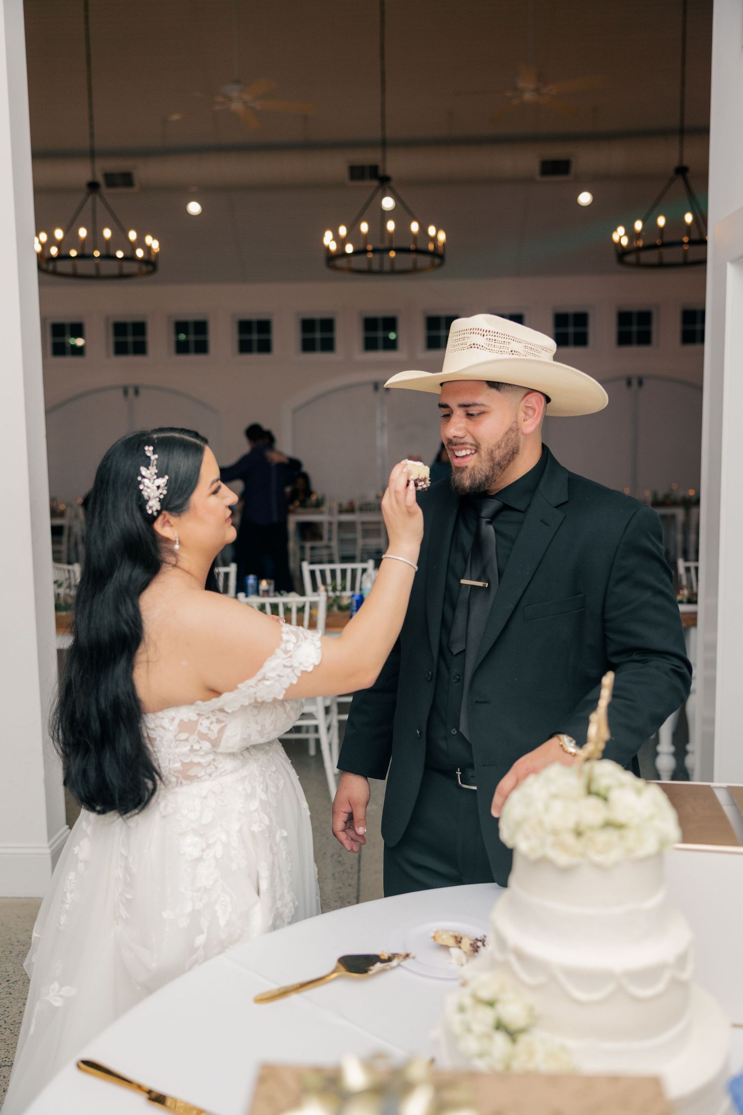 Playful cake-cutting moment between newlyweds in an elegant venue with chandeliers.