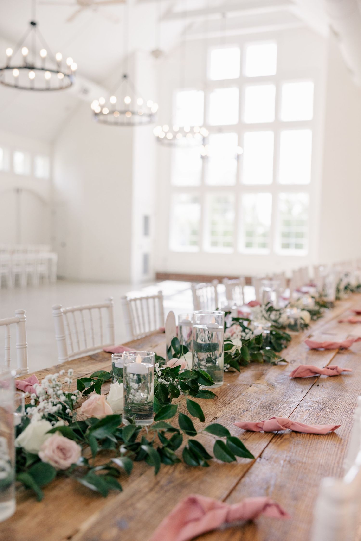 Long wooden farm table decorated with pink flowers and greenery garland for an elegant wedding reception.