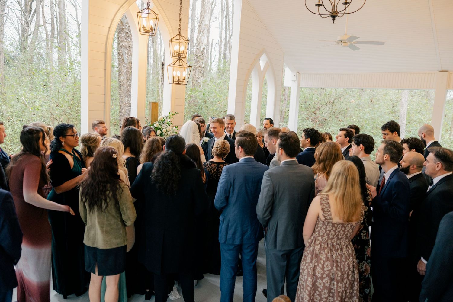 Wedding guests mingle during reception in an elegant venue with large windows.