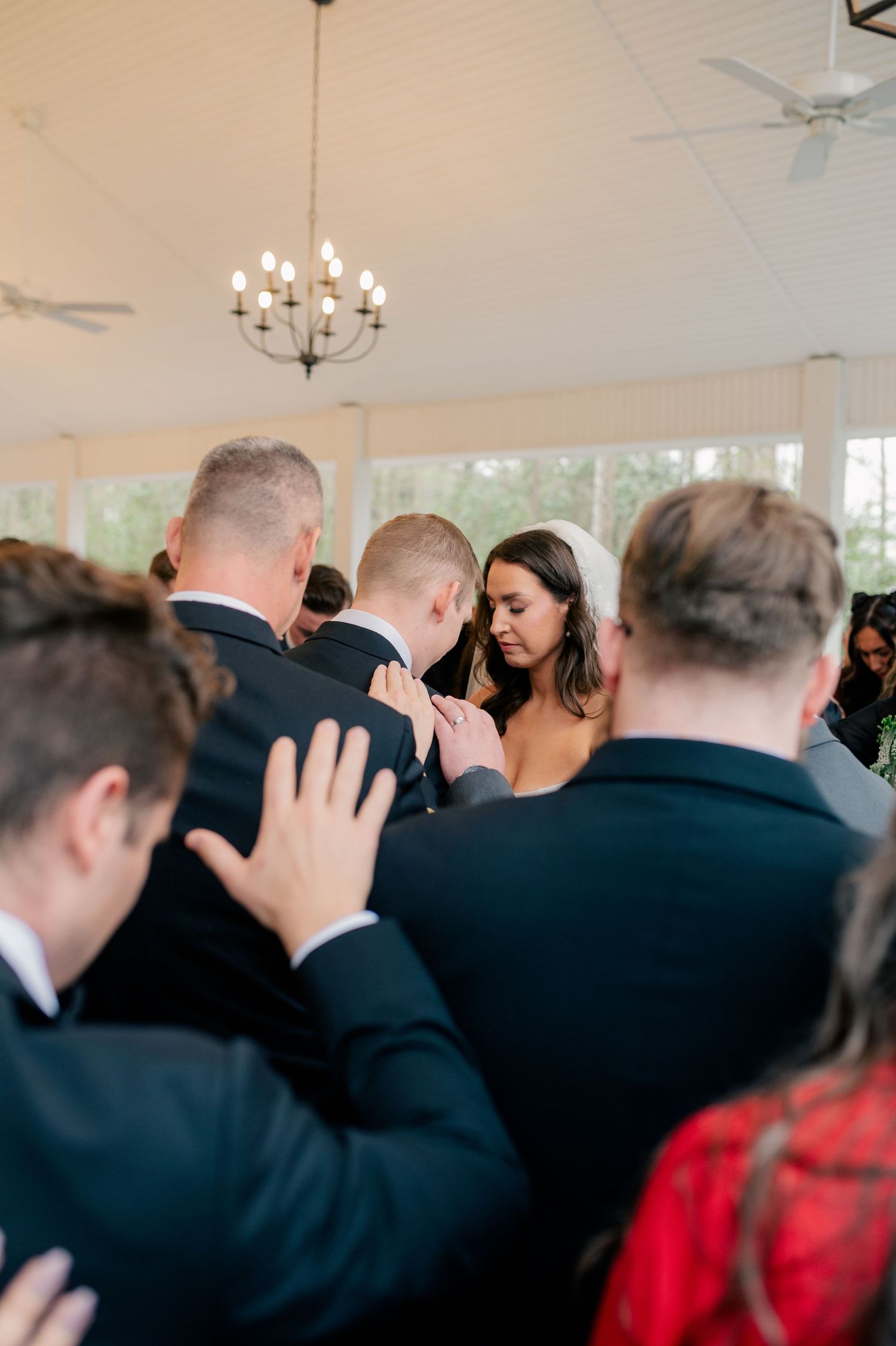 Crowd of wedding guests during ceremony in white-walled venue with chandelier.
