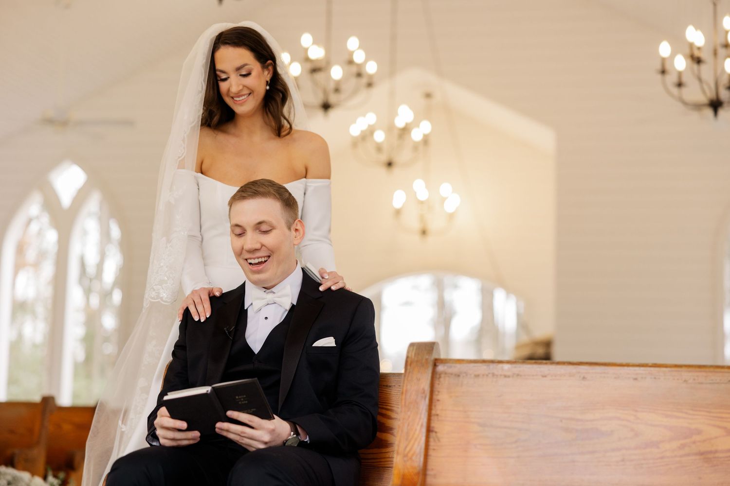 Couple shares a tender moment while reading in church with arched windows and chandeliers.