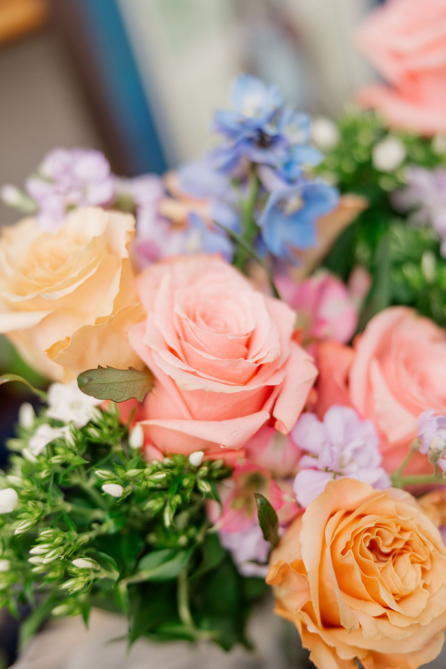 Delicate peach and pink roses with small purple flowers arranged in an elegant floral display.
