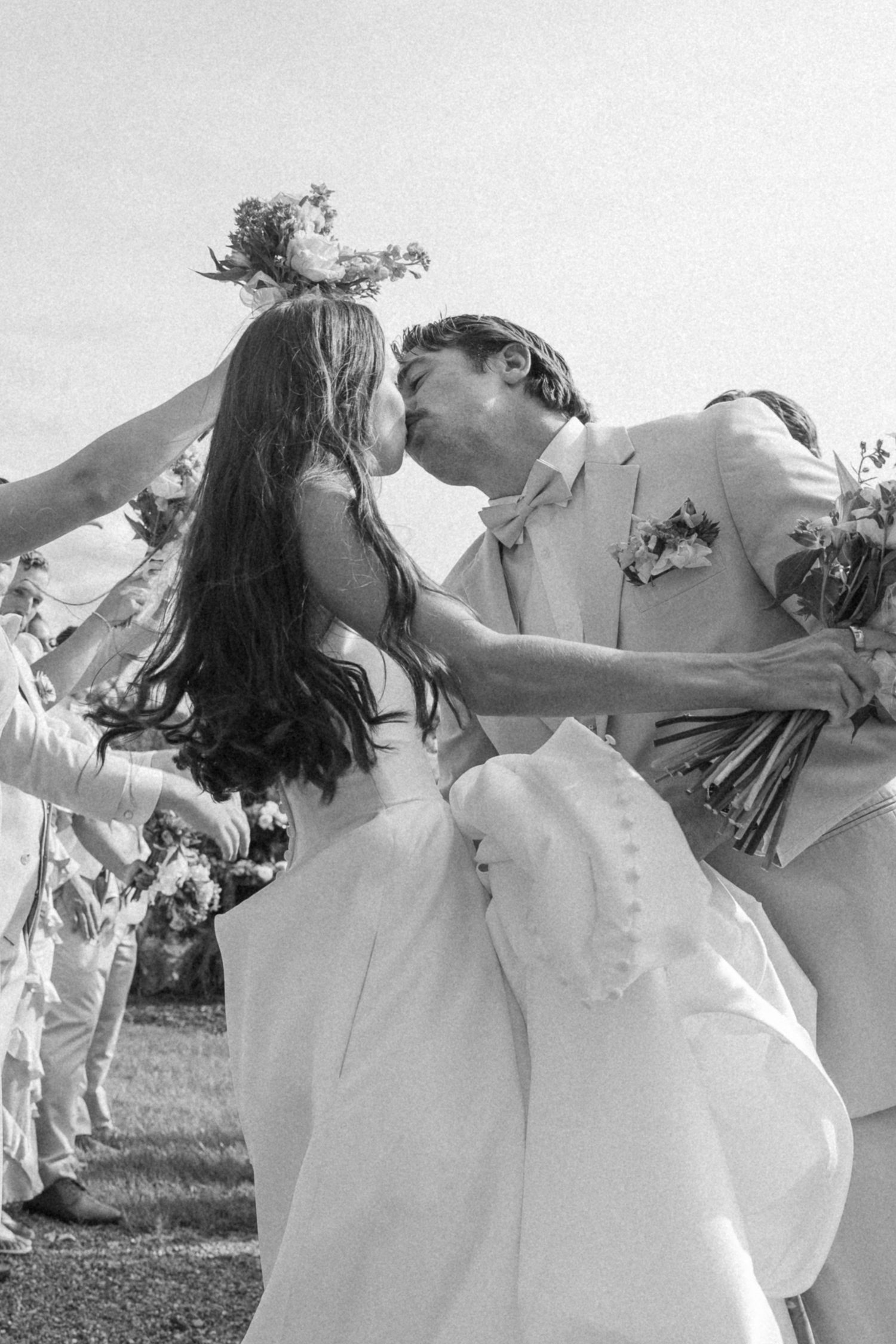 Wedding party in white outfits performs choreographed dance moves in a field.