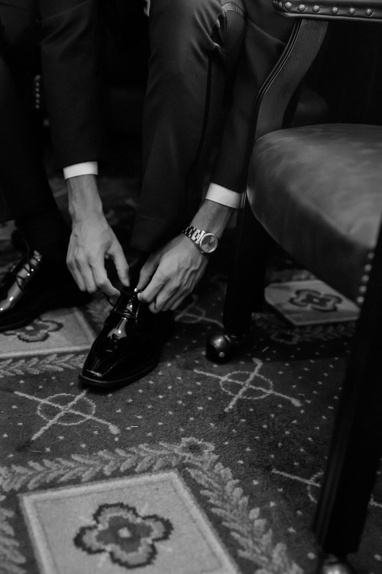 Black and white photo of dress shoes on a patterned carpet showing formal attire details.