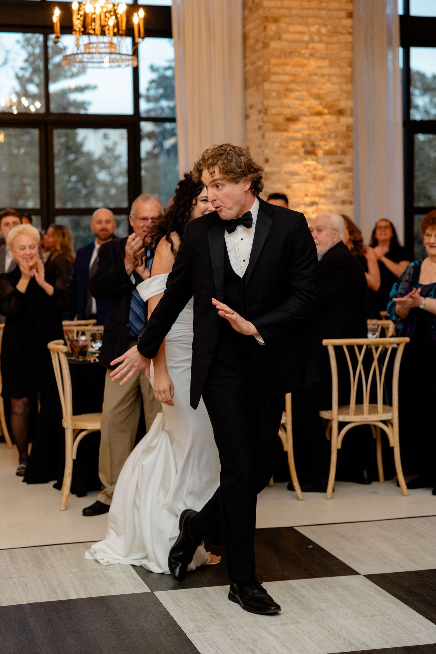 A spirited dance performance at an elegant wedding reception with exposed brick walls and chandeliers.