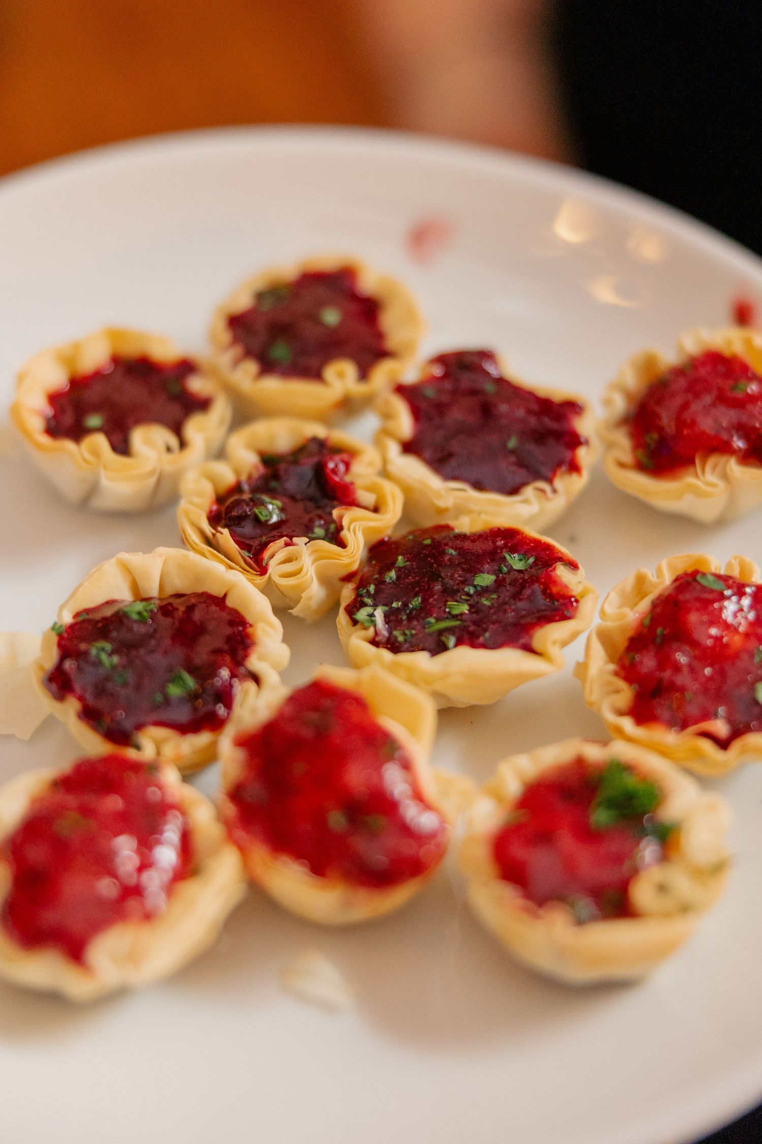 Plate of bite-sized phyllo pastry cups filled with red berry jam garnished with fresh herbs.