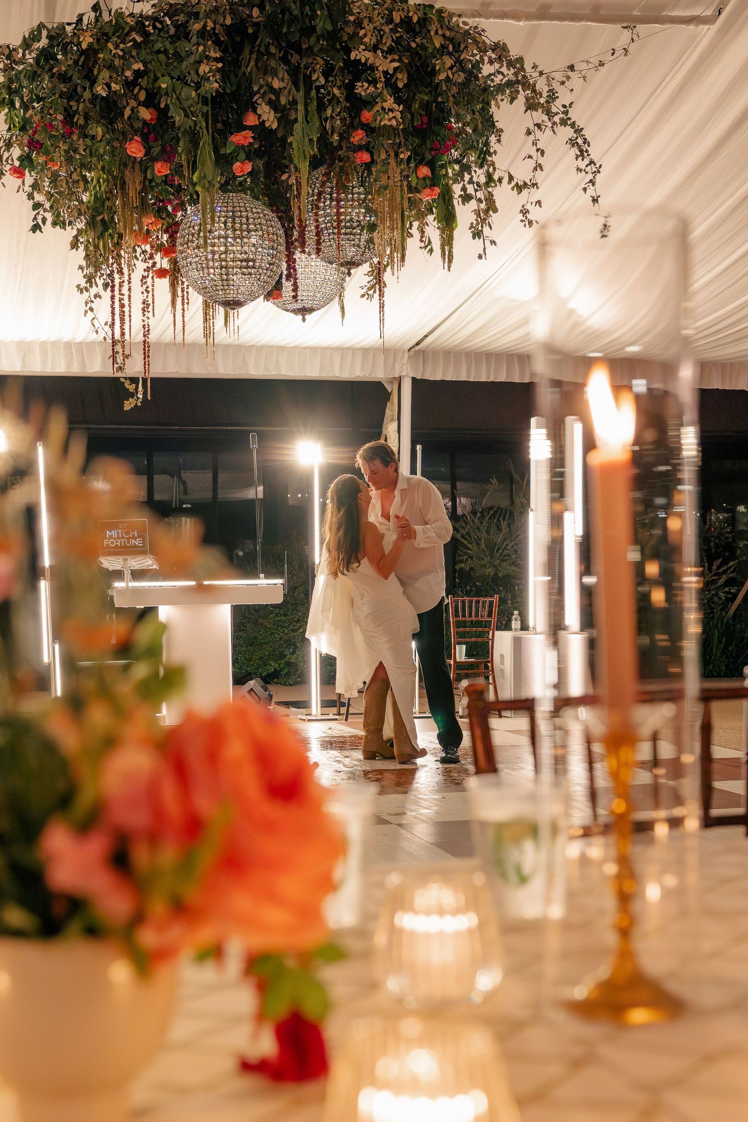 Couple shares romantic first dance under floral chandelier with candles and warm lighting at wedding reception.