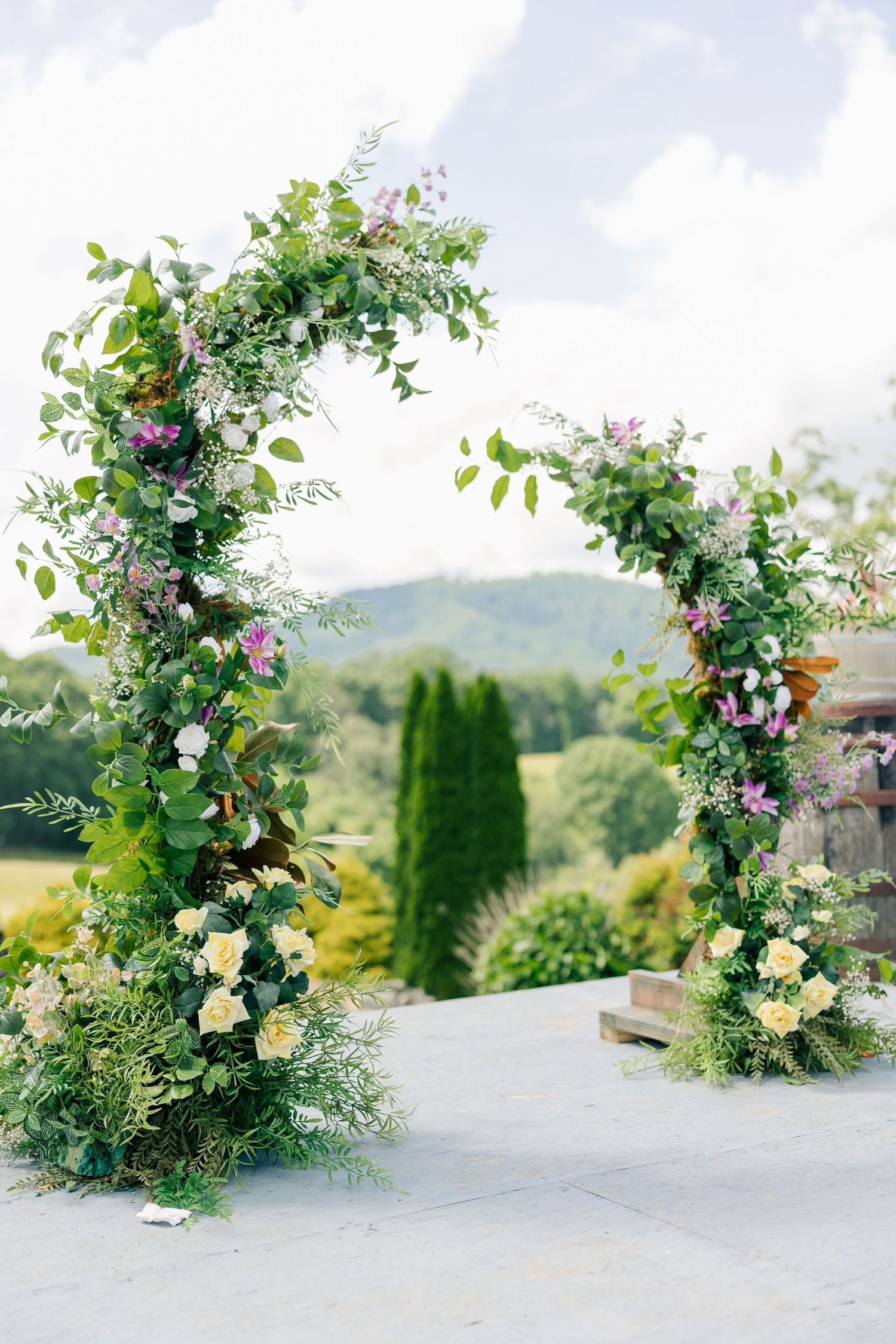 Beautiful floral wedding arch with greenery and roses frames a mountaintop view at an outdoor ceremony venue.