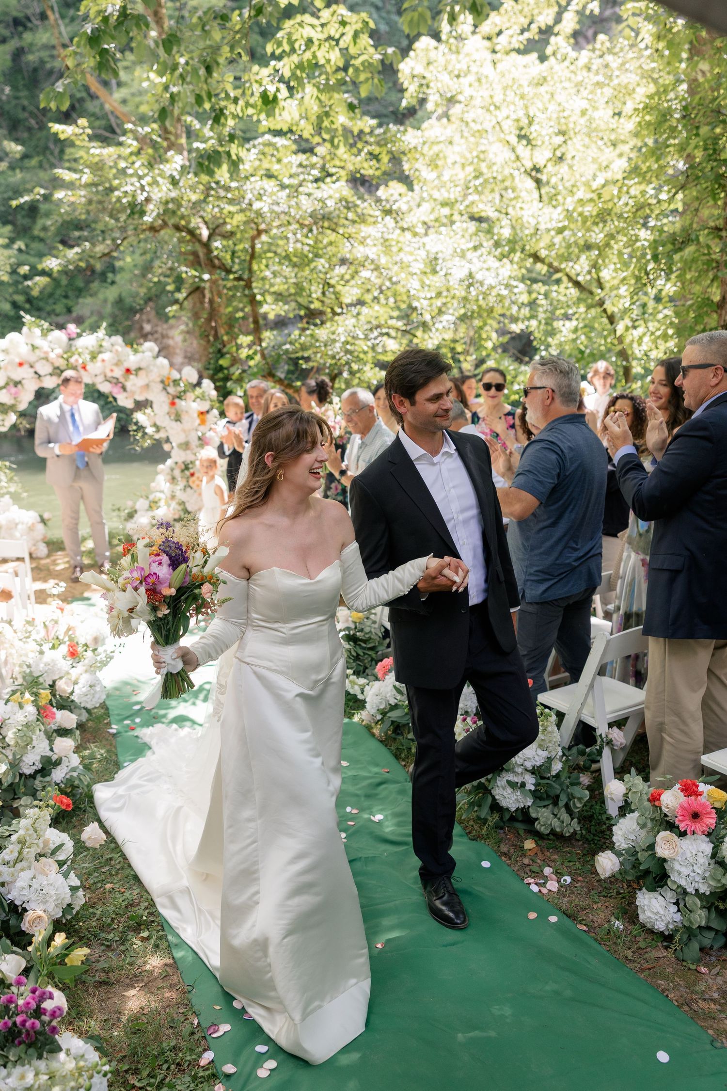 Newlyweds walk hand in hand down floral-lined aisle after outdoor wedding ceremony.