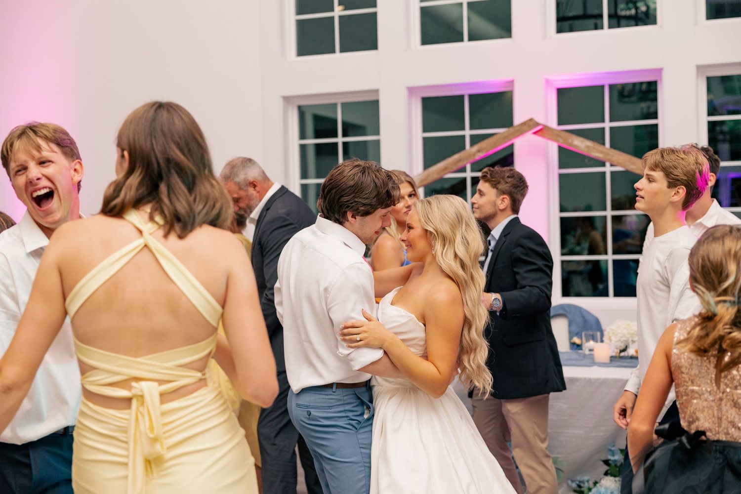 Bride and groom share a kiss surrounded by dancing guests at their wedding reception.