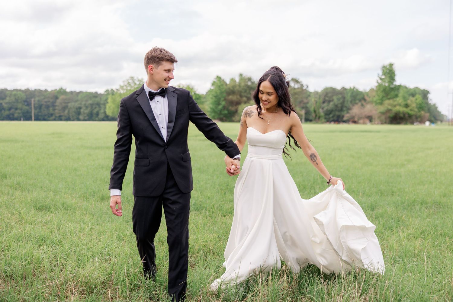 A joyful couple strolls through a meadow in their wedding attire.
