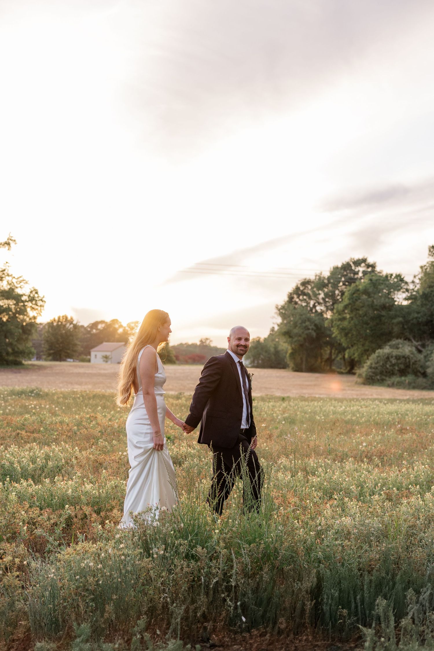 Wedding couple walking through a sunlit meadow at golden hour.