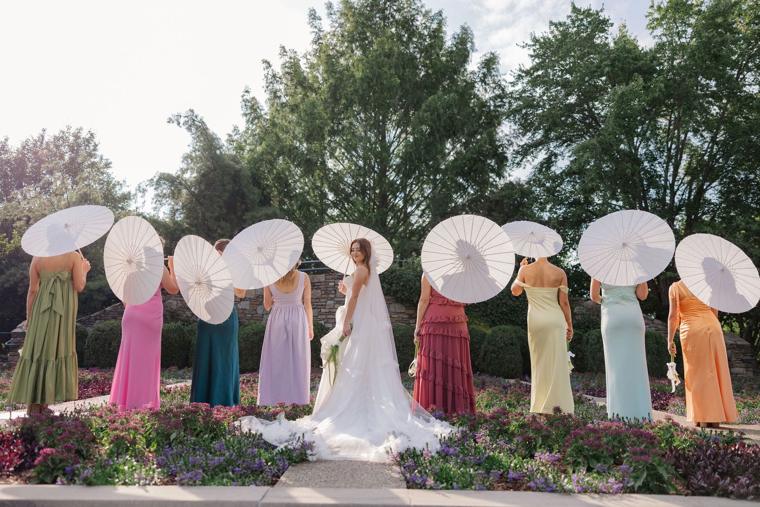 Wedding party holding white parasols in a garden setting.