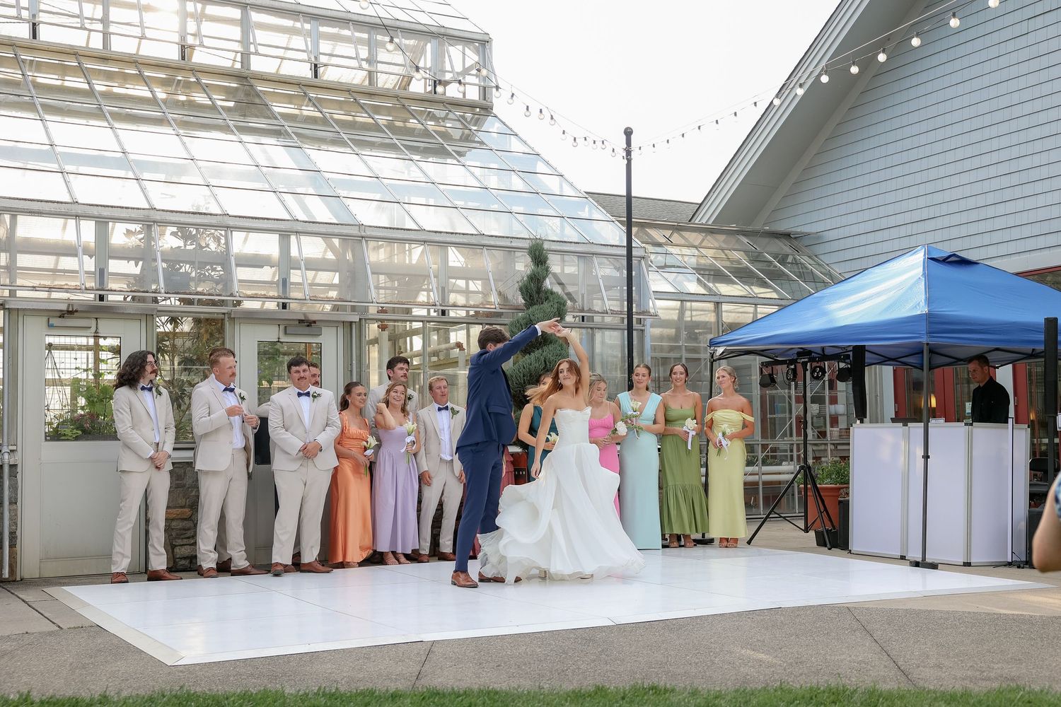 Wedding reception setup under a large greenhouse structure with white tables and chairs.