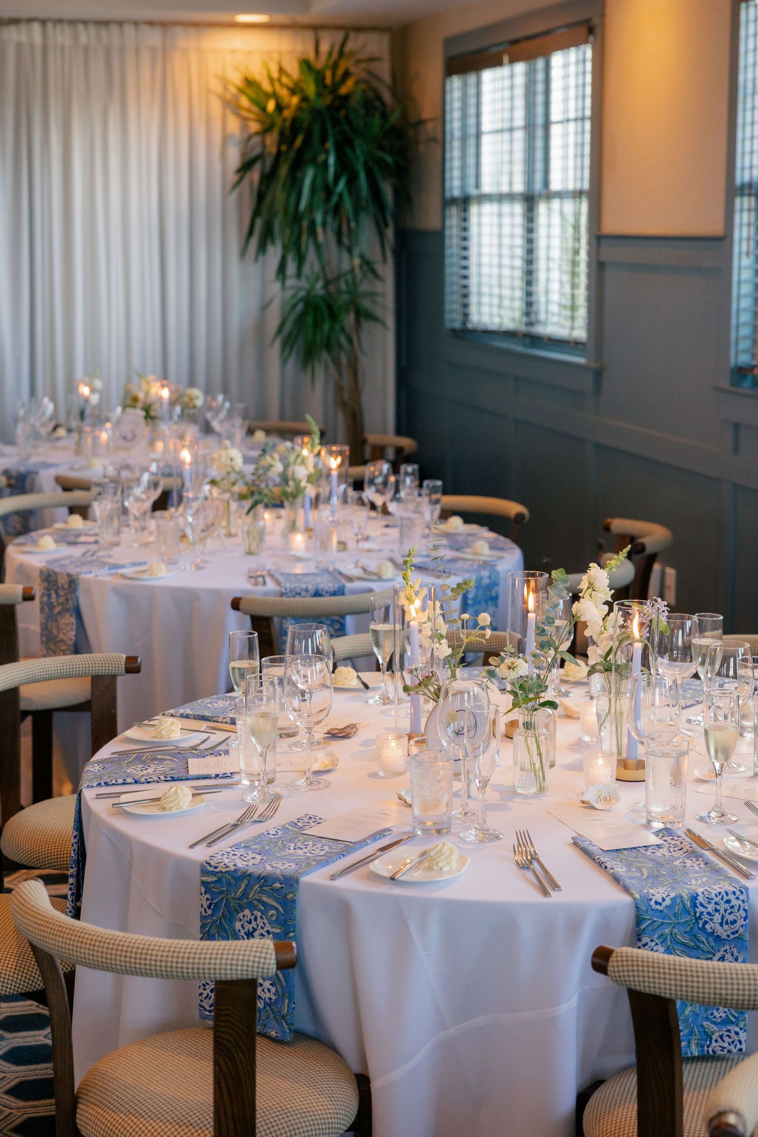 Elegant wedding reception tables with blue floral napkins, white linens, candles, and floral centerpieces.