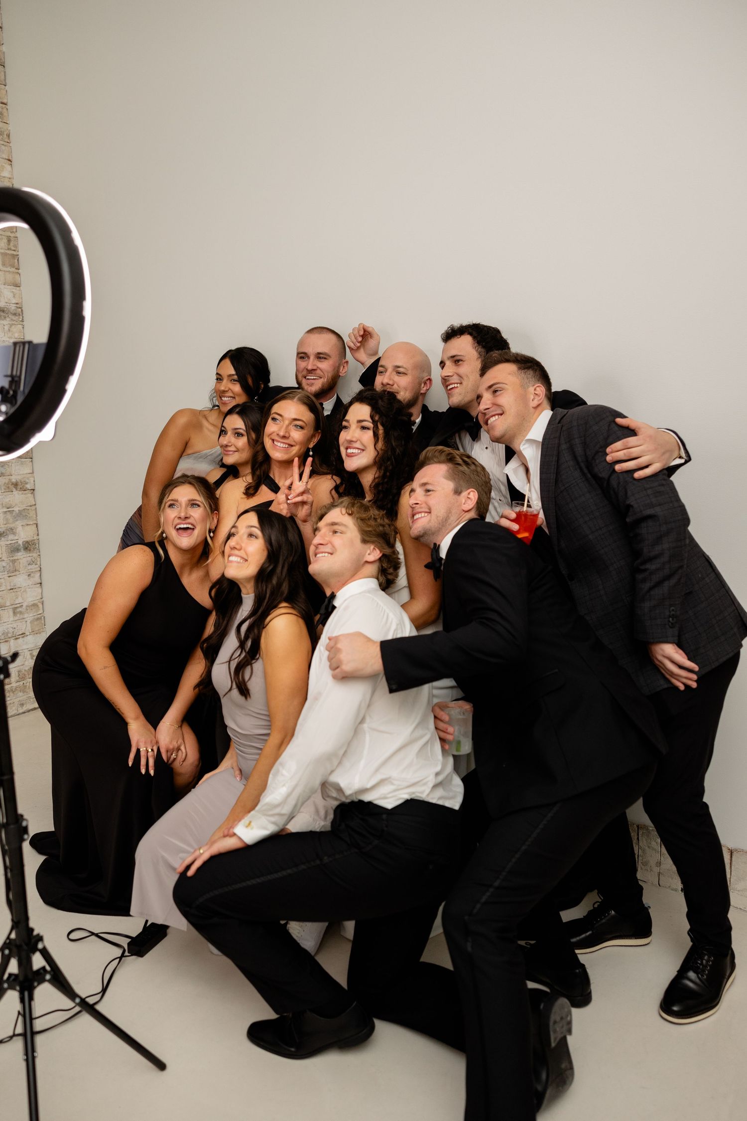 Wedding party poses together for fun group photo in formal attire against white studio backdrop.
