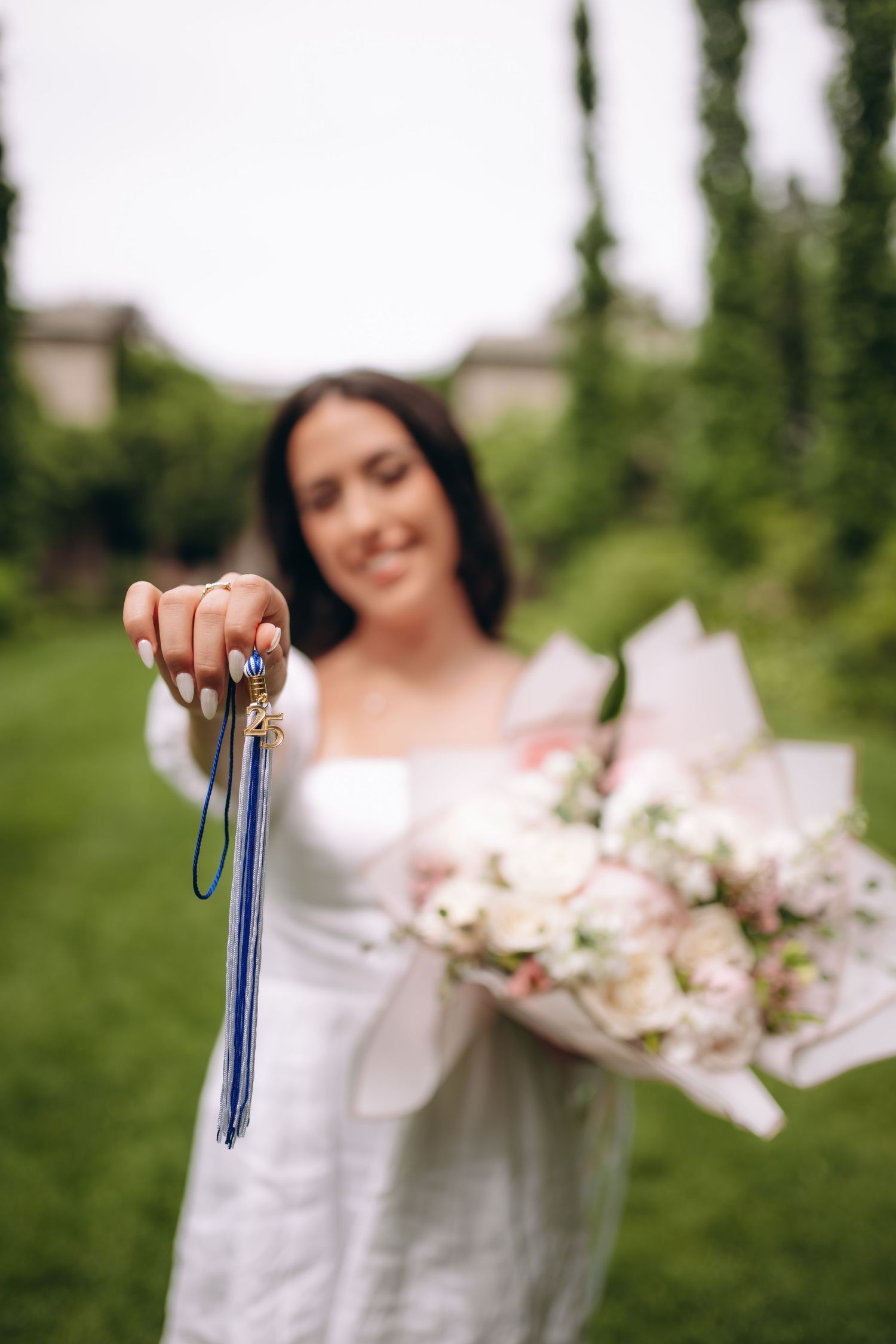 A person in white dress holds keys while carrying a delicate pink and white flower bouquet in an outdoor garden setting.
